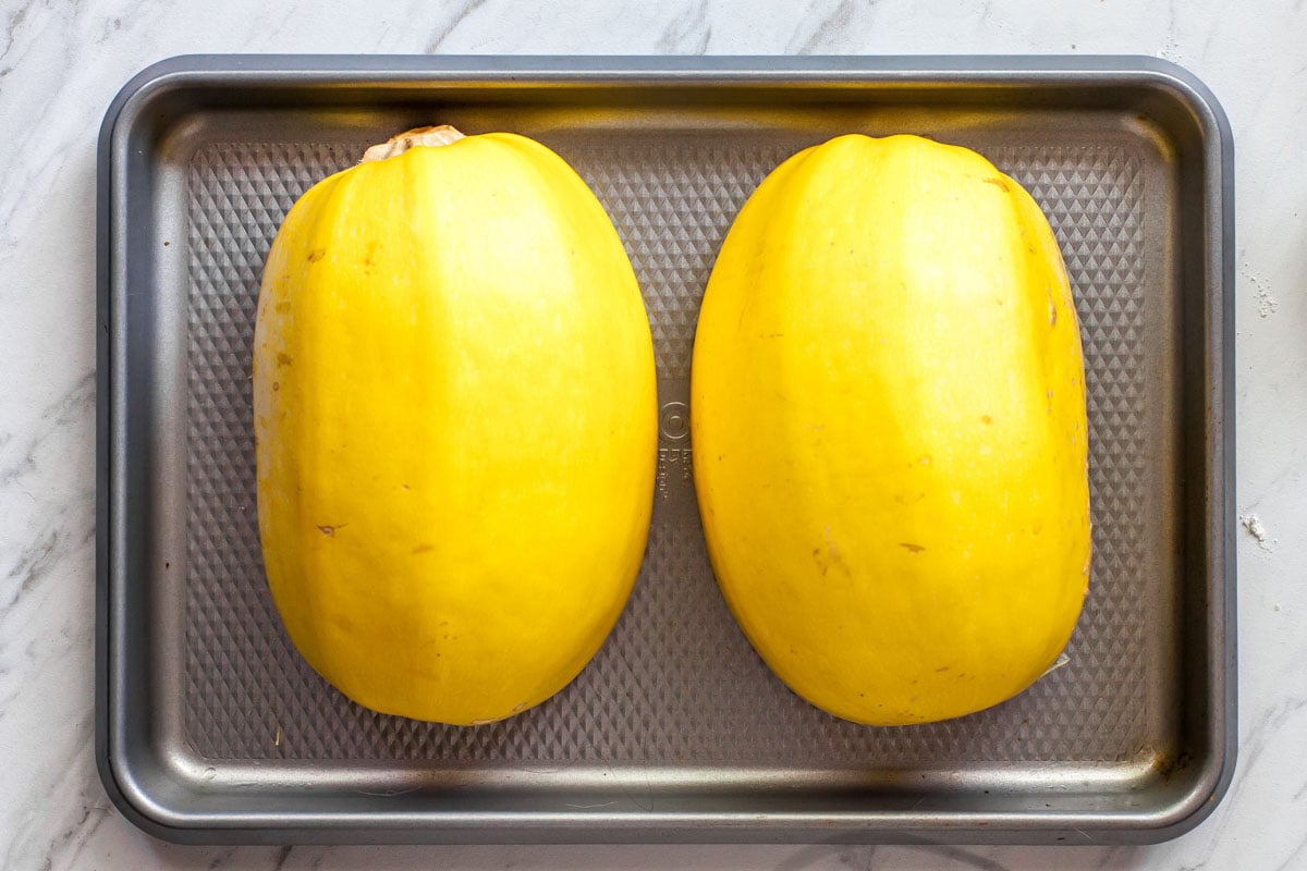 Two spaghetti squash halves flesh side-down on a silver baking sheet