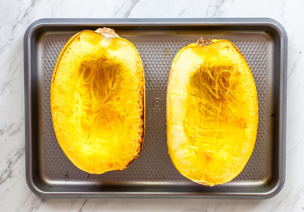 Two spaghetti squash halves facing up on a silver baking sheet