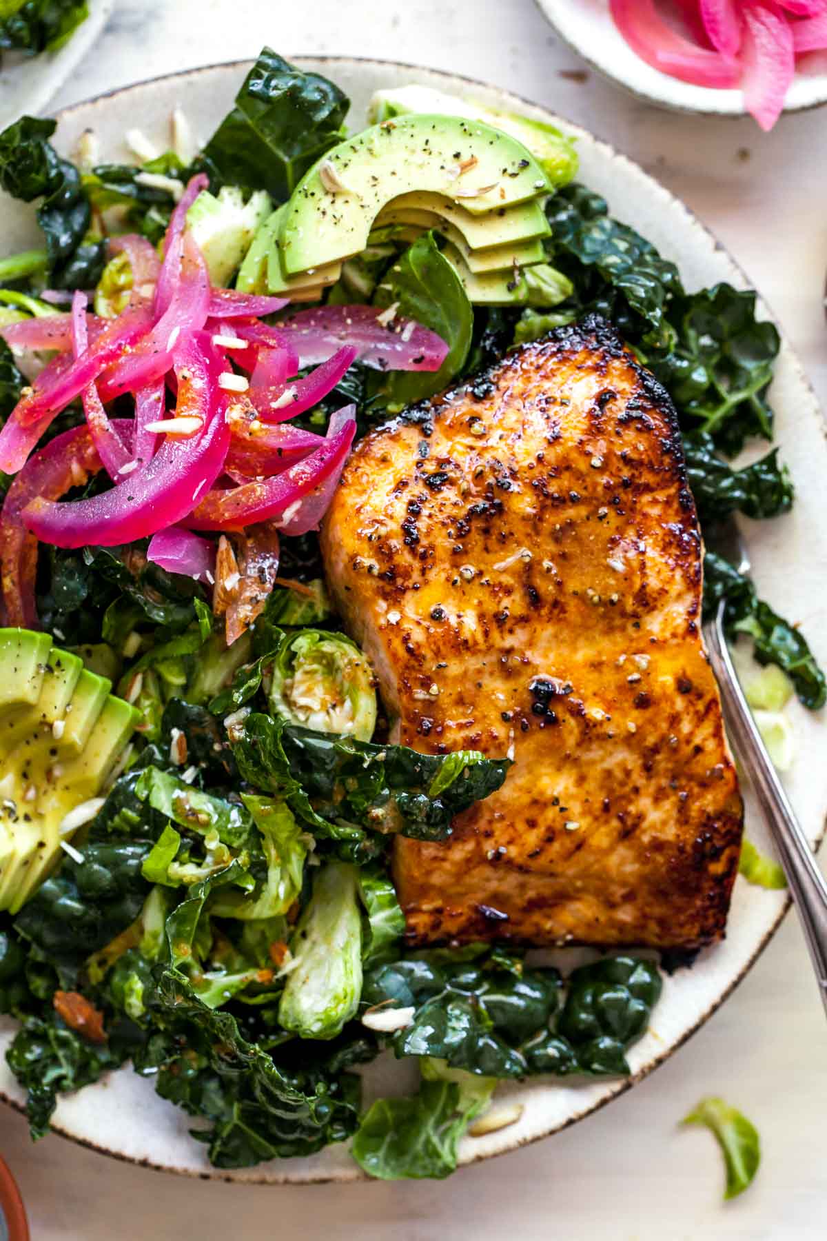 Close up view of cooked salmon fillet over kale salad with pickled red onion on top