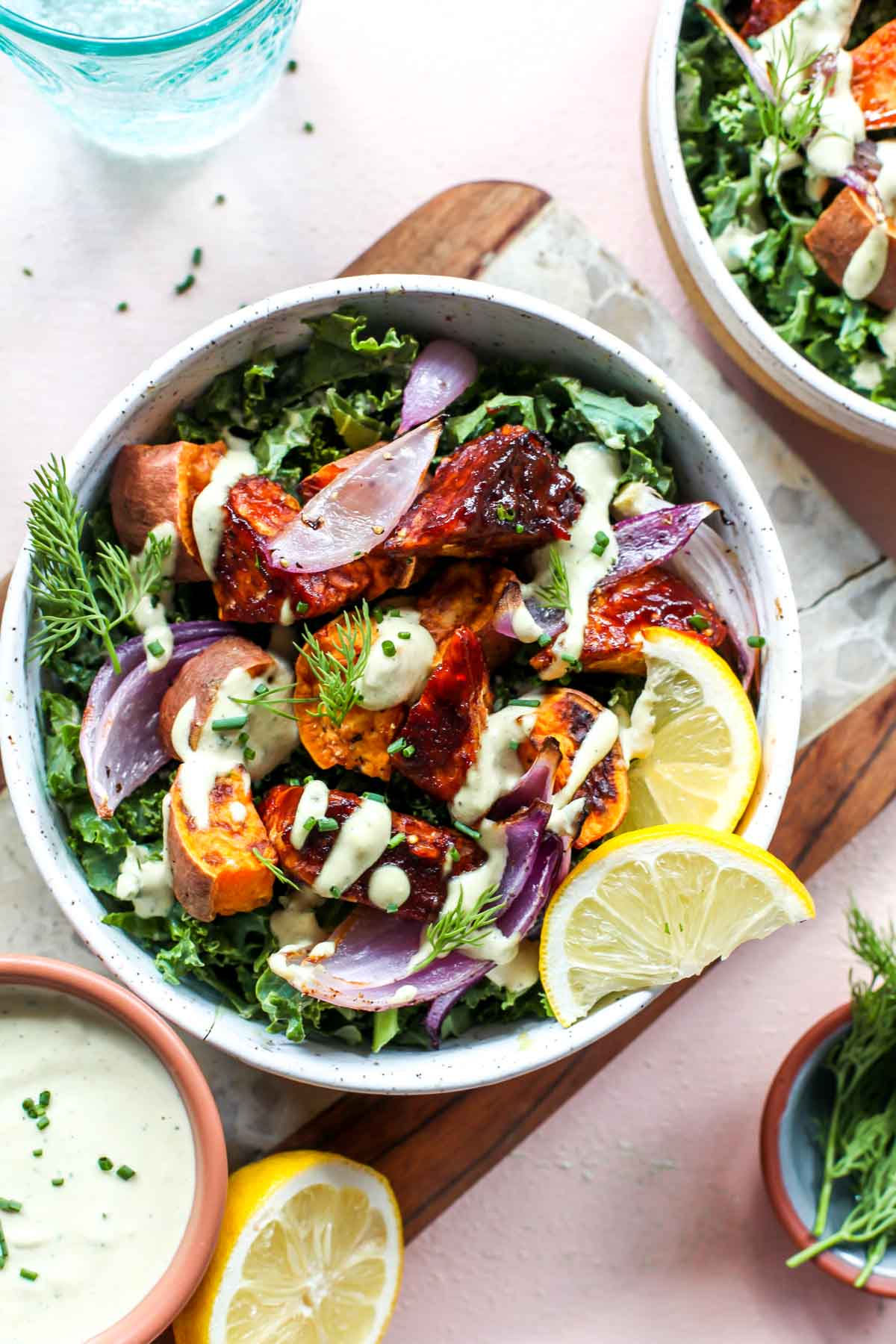BBQ tempeh over massaged kale in a white bowl topped with lemon wedges
