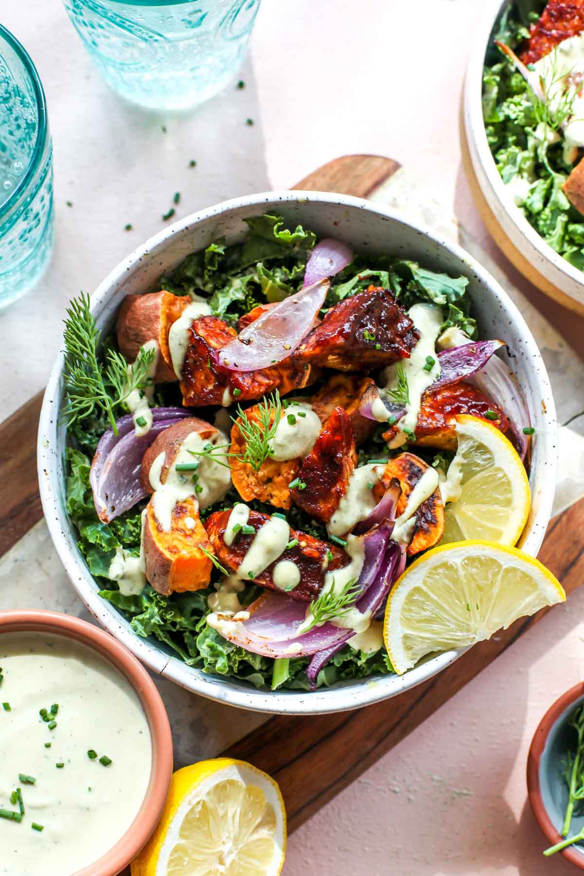 Kale, red onion, and bbq tempeh in a white bowl on a tan cutting board