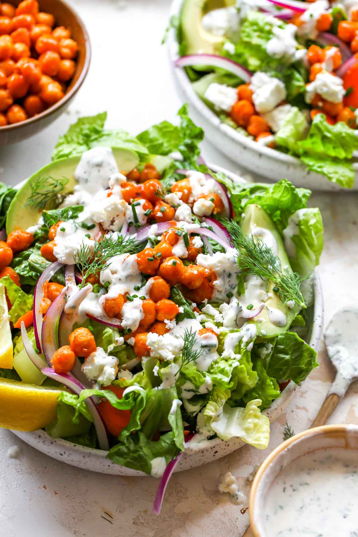Side angle of buffalo chickpea salad in a white bowl topped with avocado