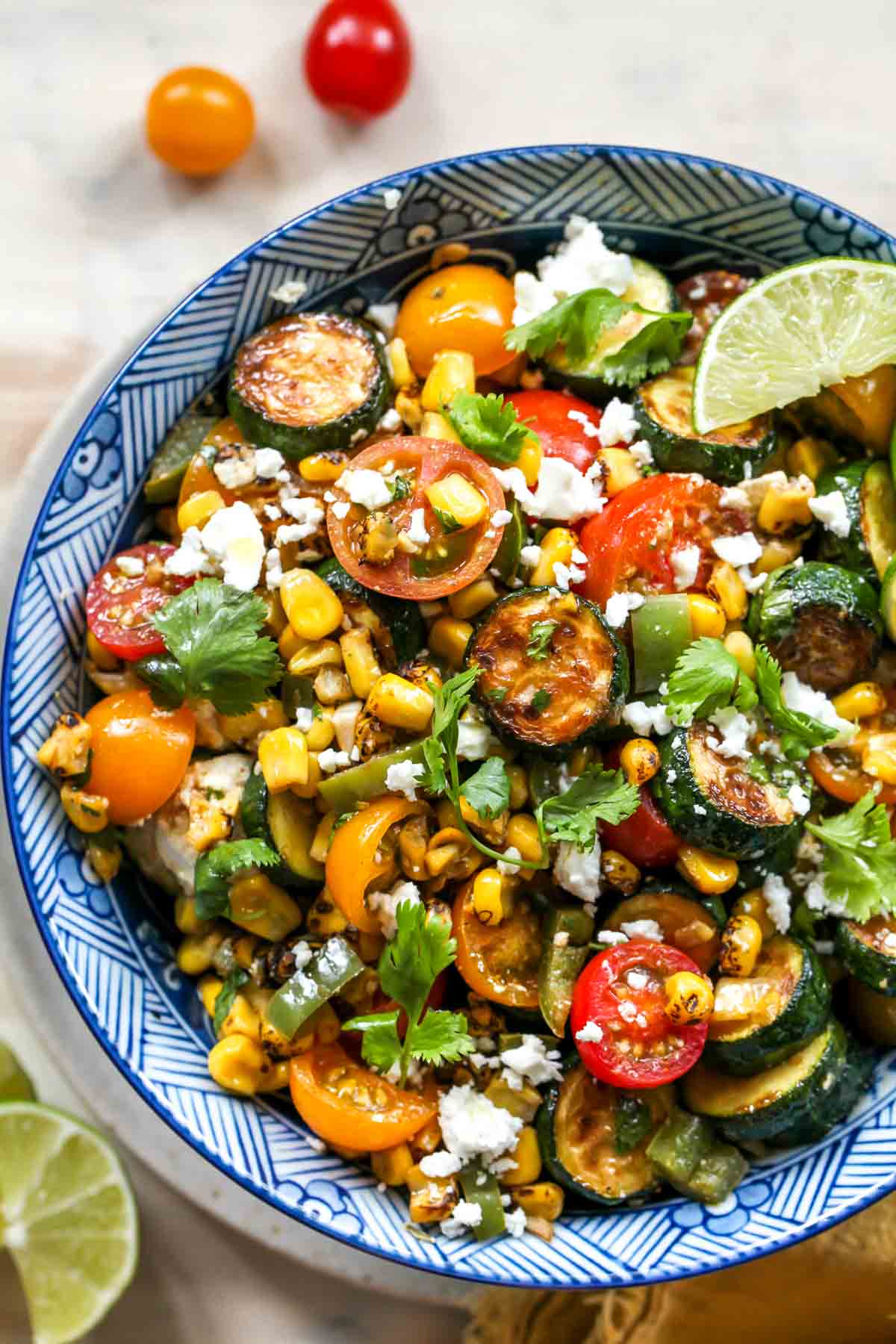 Corn, zucchini, and tomatoes in a blue bowl topped with feta cheese