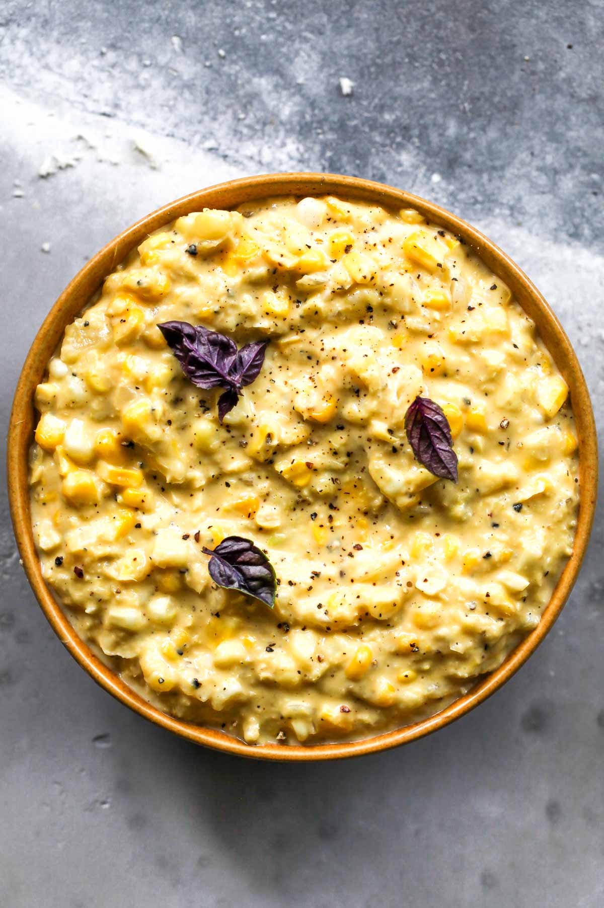 Creamed corn in a yellow bowl topped with purple basil leaves