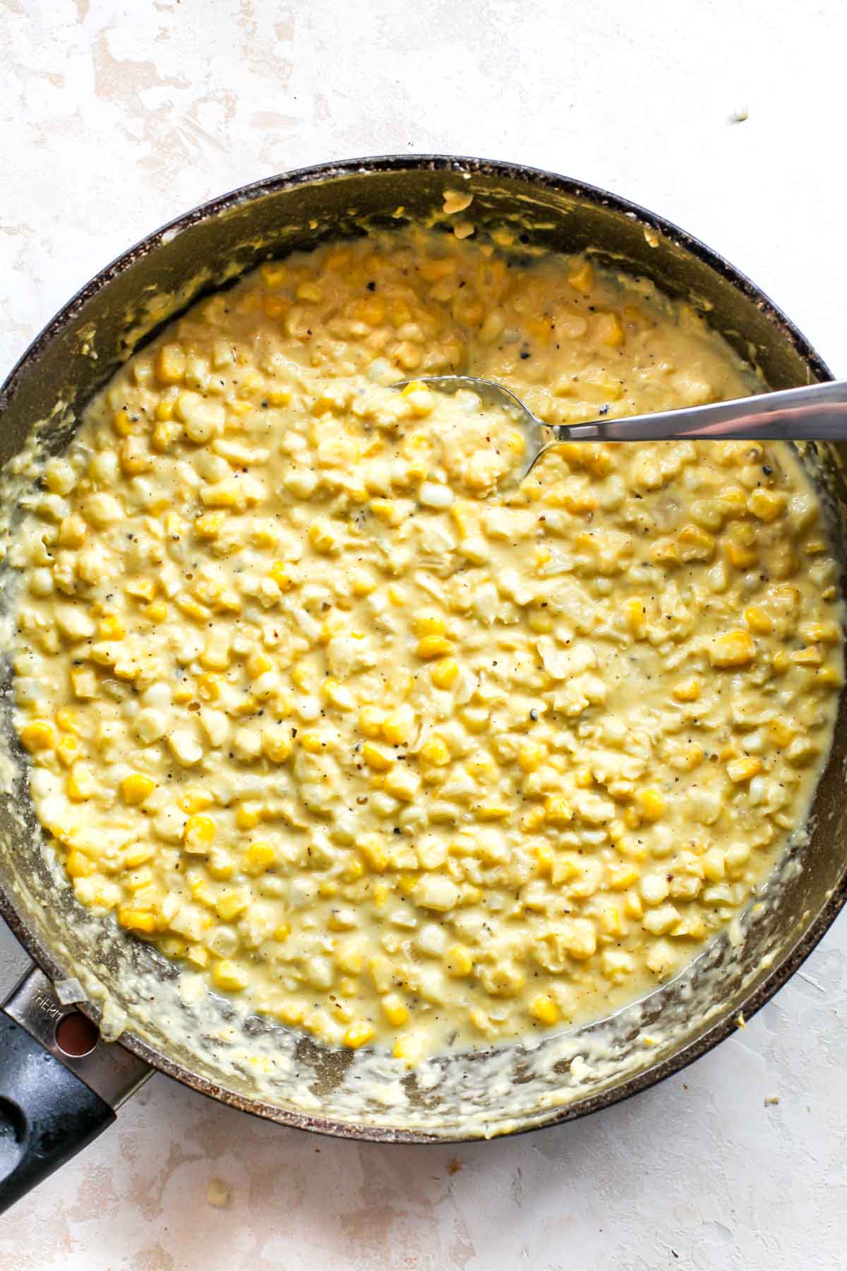 Creamed corn in a large skillet with spoon resting on the right side