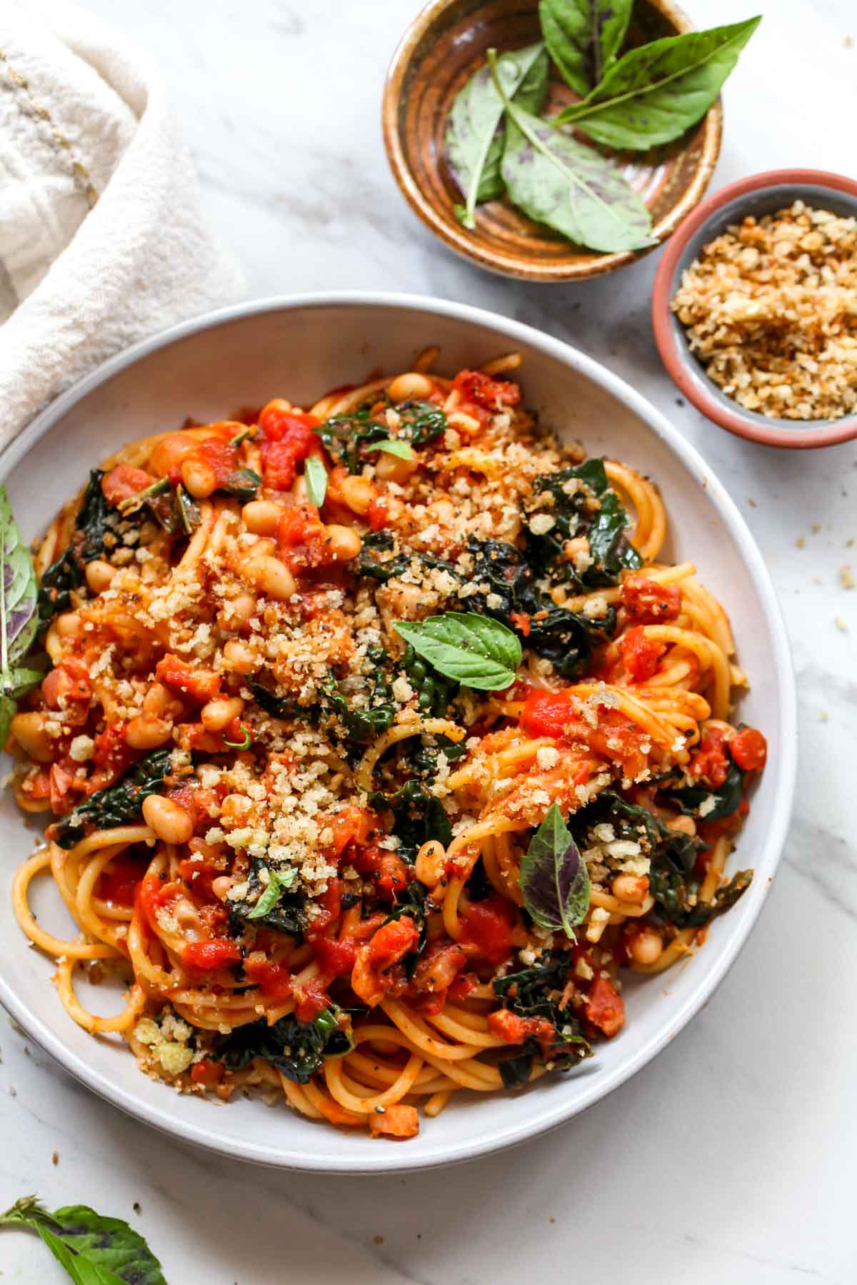 Spaghetti in red sauce with kale on a gray plate topped with breadcrumbs