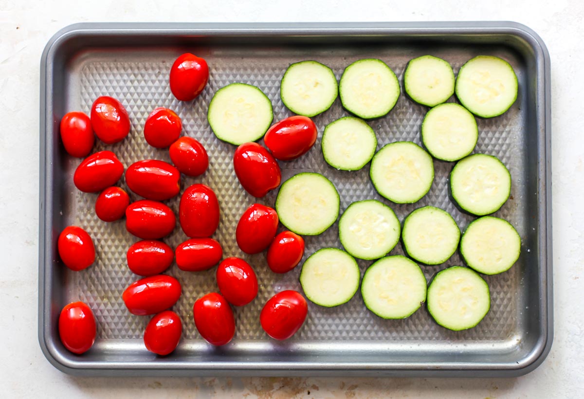 Sliced zucchini and tomatoes on a large baking sheet