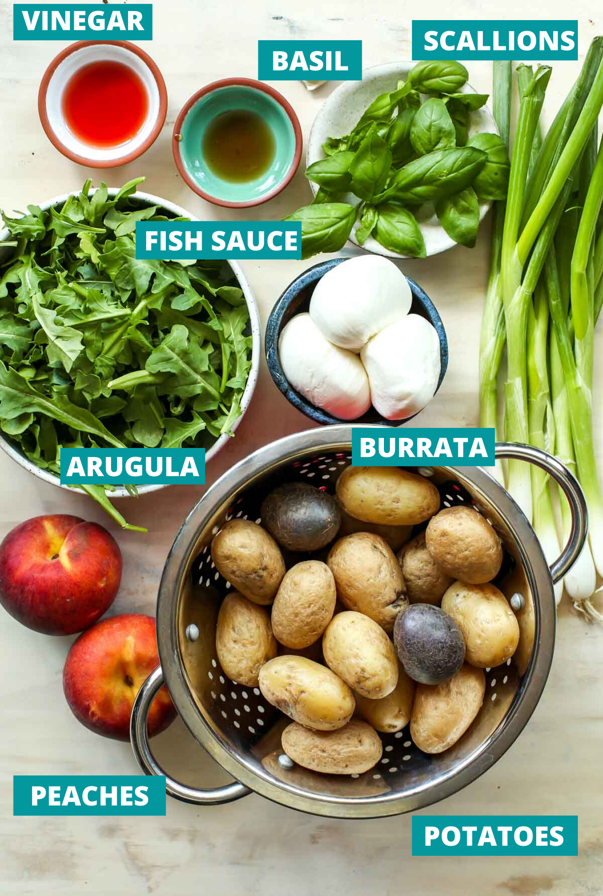 Baby potatoes, arugula, peaches, and burrata in separate bowls on a white surface with ingredient tags.