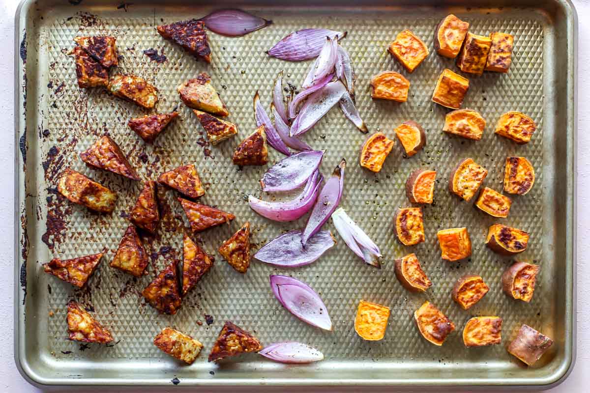 Tempeh, red onion, and cubed sweet potato separated on a baking sheet