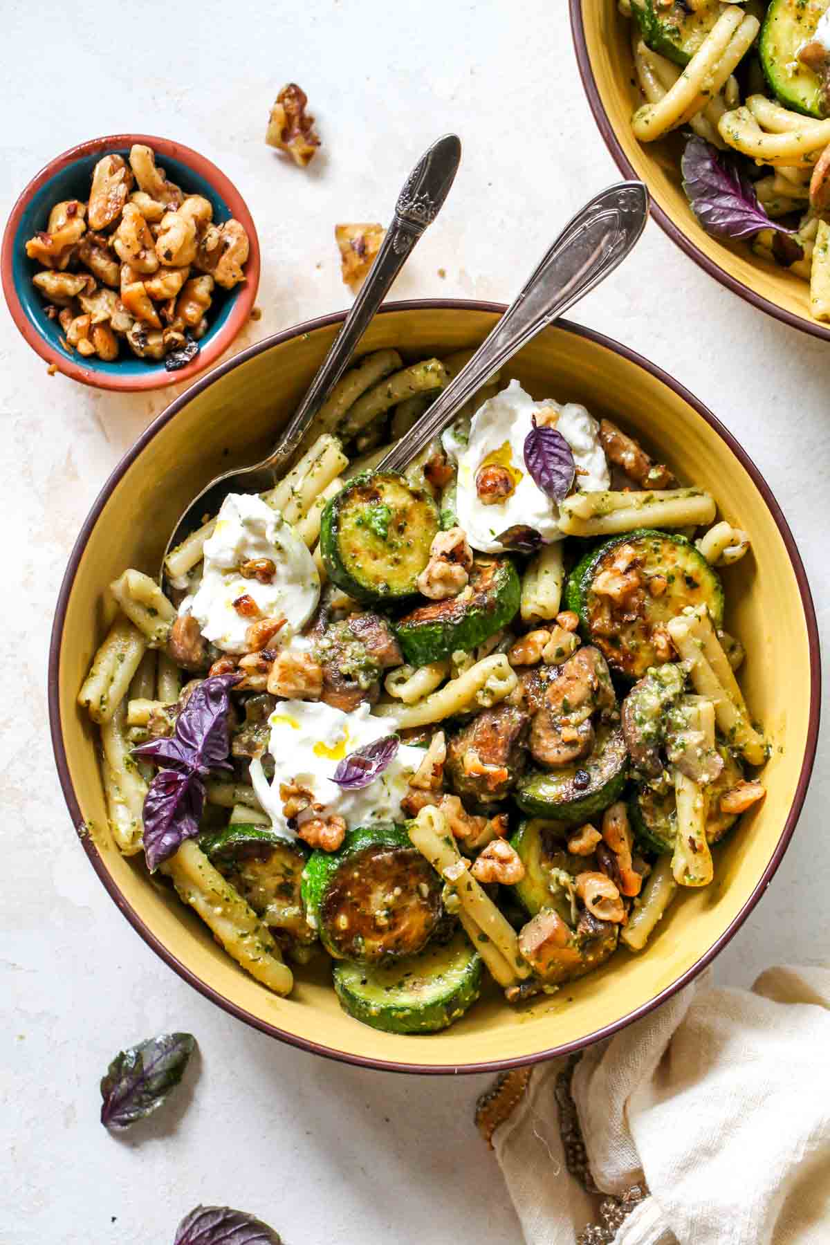Pesto pasta in a yellow bowl with zucchini and mushrooms.