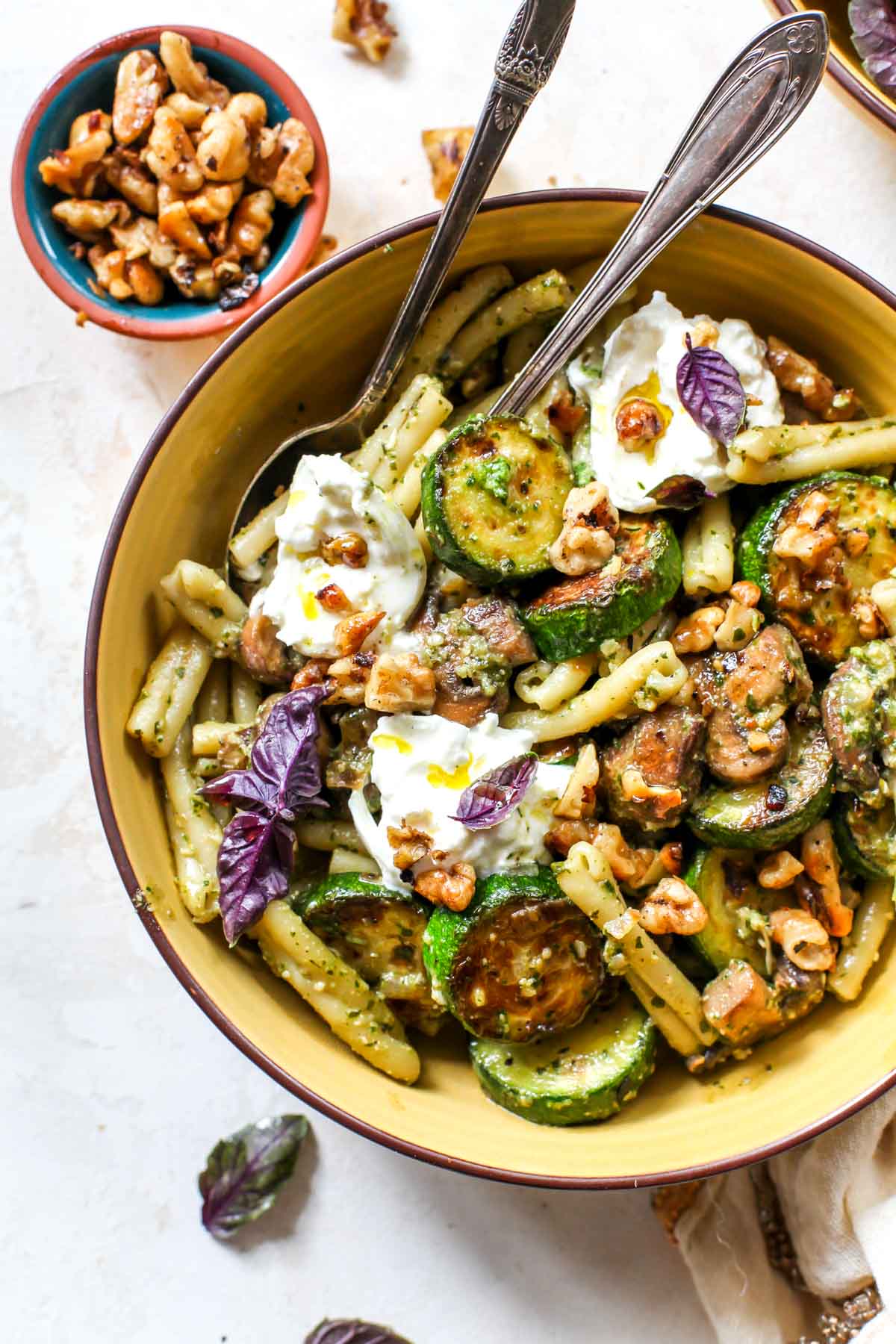 zucchini pesto pasta with buttery mushrooms and walnuts styled in a yellow pasta bowl.