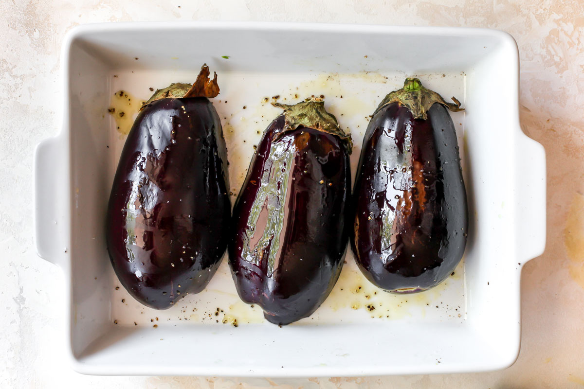 Eggplant halves flesh side down in a white baking pan