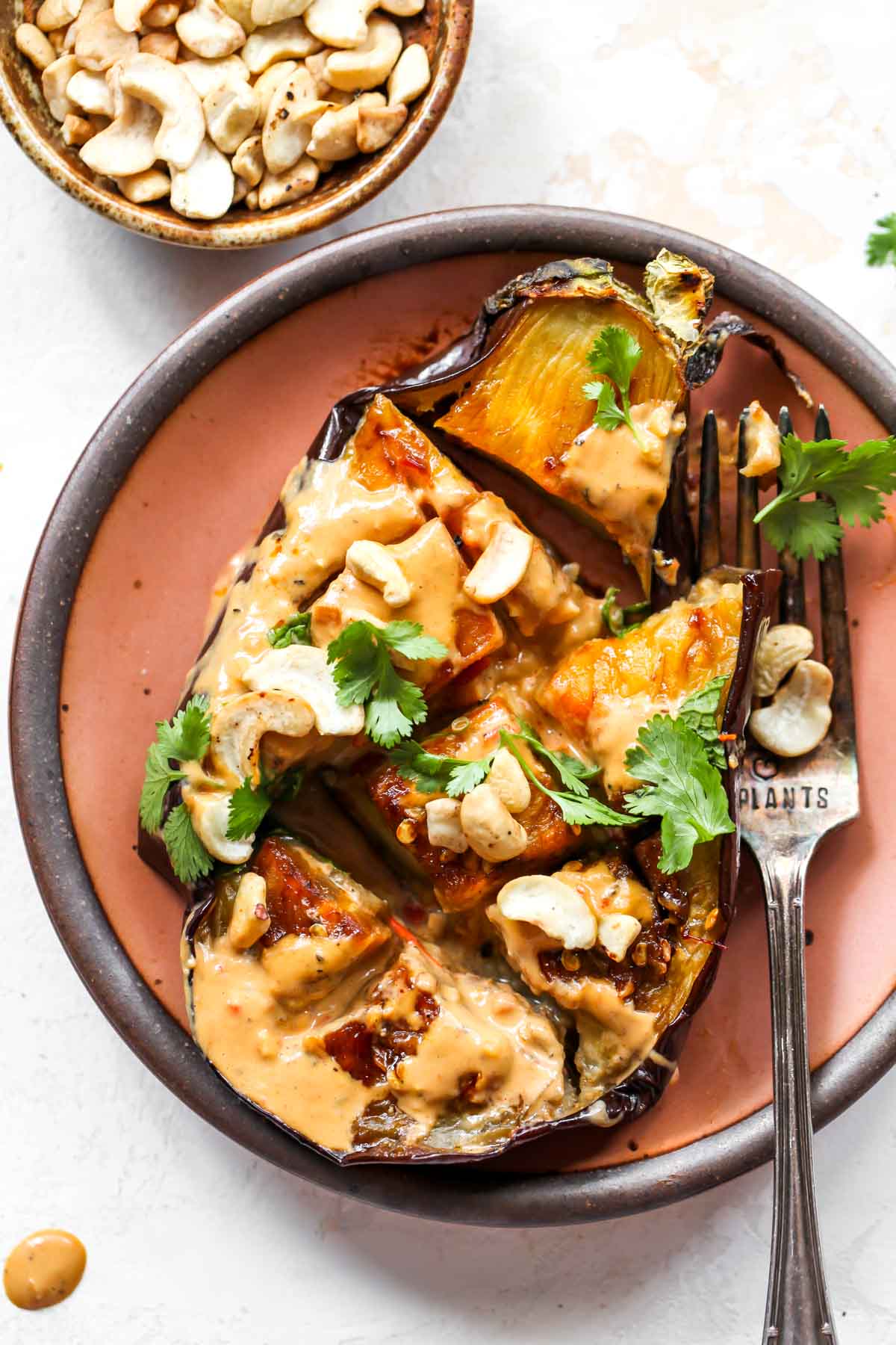 One eggplant half on a pink plate with a fork resting on the side