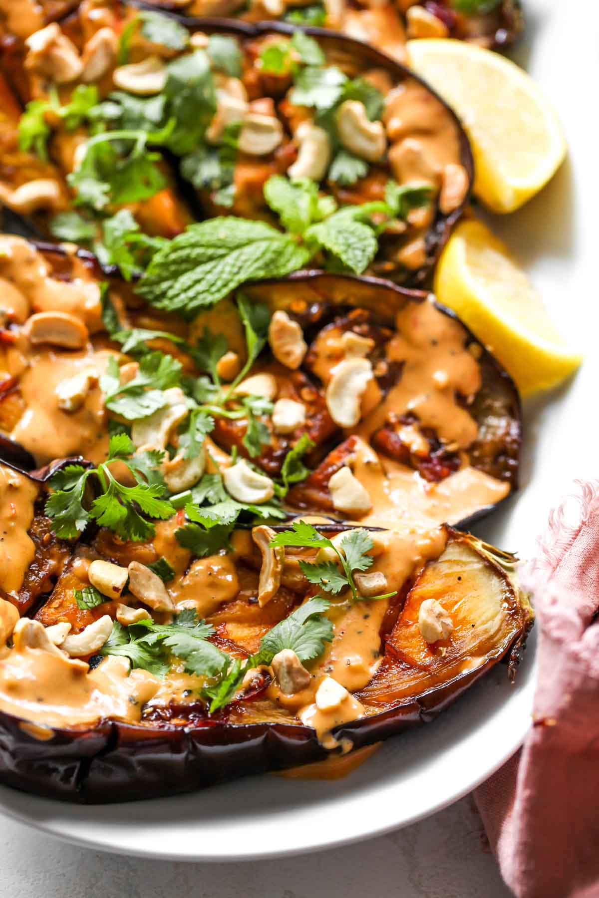 Roasted eggplant on a white platter topped with harissa-tahini sauce