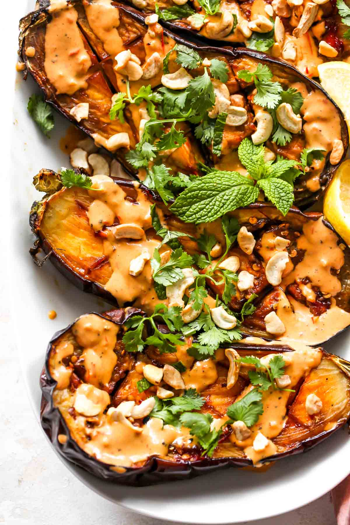 Eggplant halves on a white platter topped with cilantro and nuts