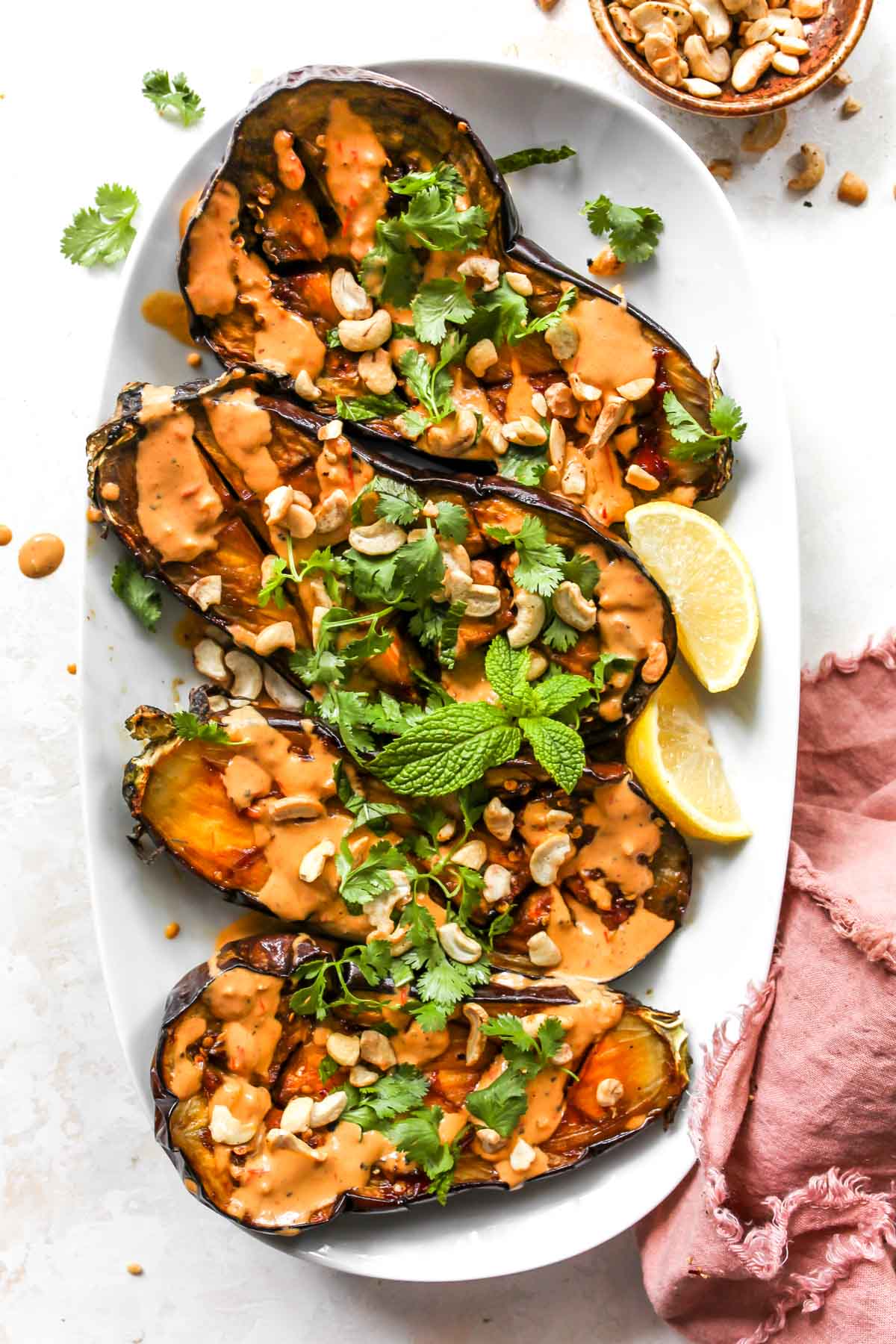 Four eggplant halves on a white platter garnished with nuts and herbs