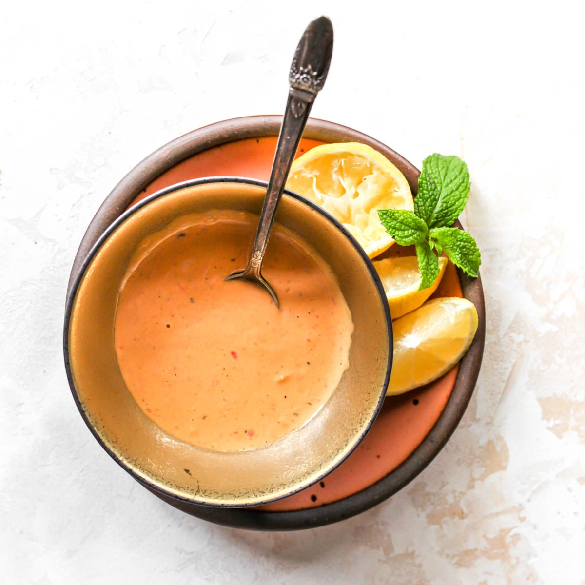 Harissa-tahini sauce in a gold bowl on a pink plate