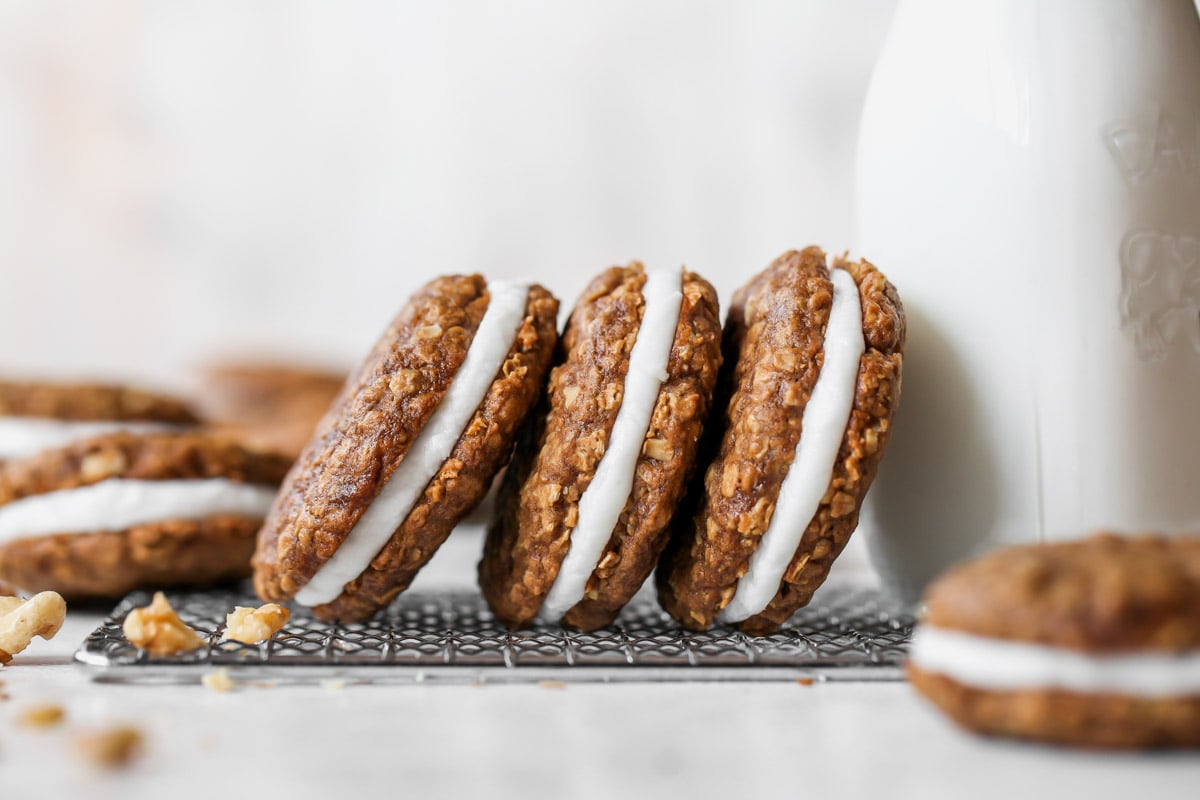 Three oatmeal creme pies on their sides leaning against a glass of milk