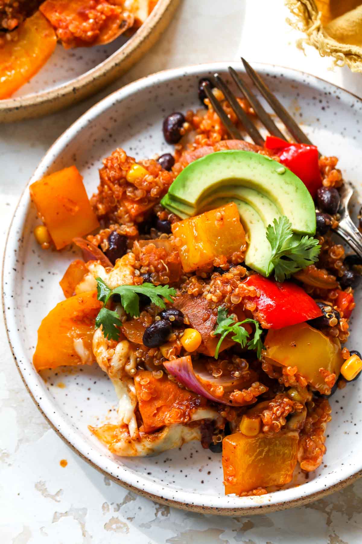 Single portion of quinoa enchilada casserole on a white plate topped with avocado slices