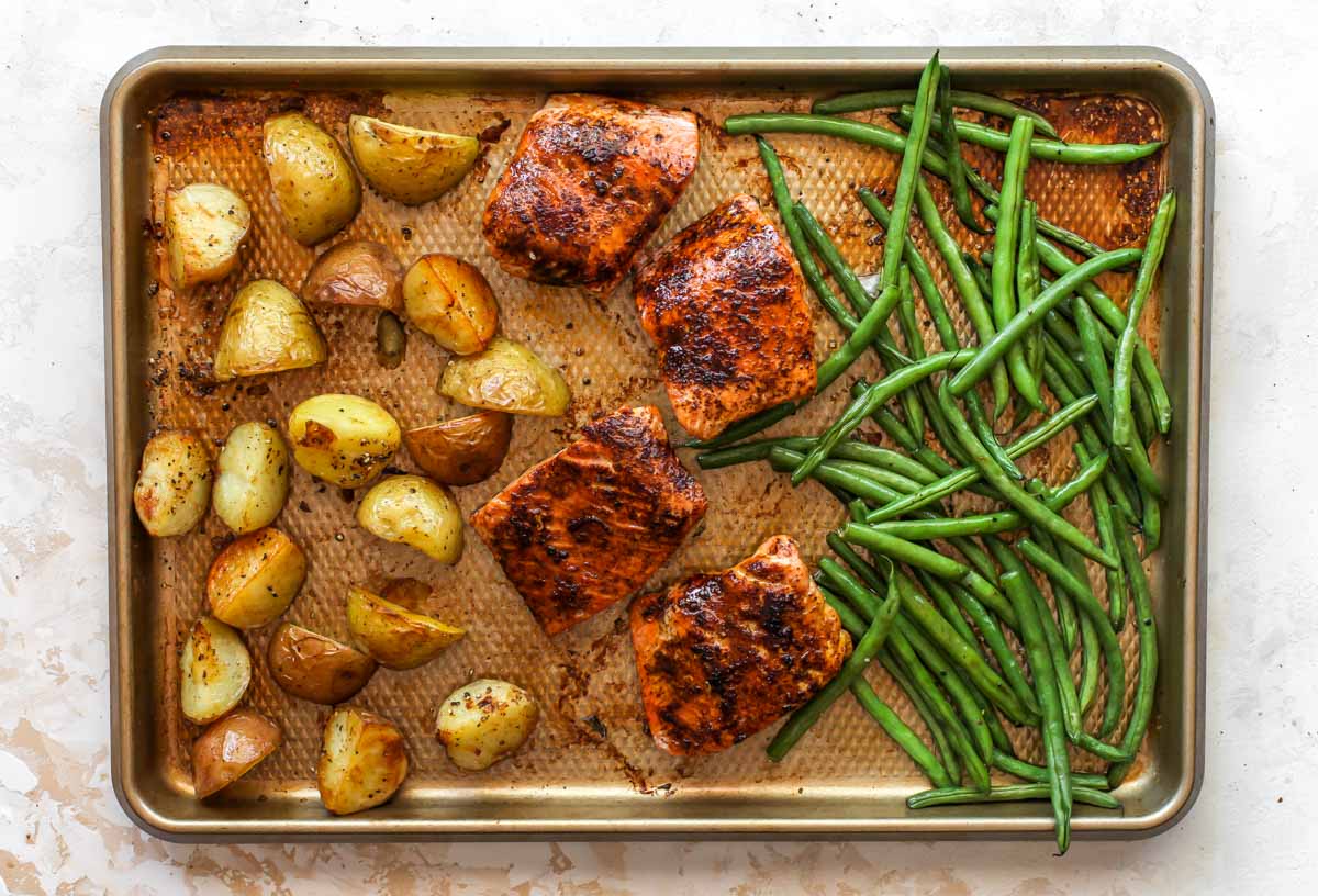 Potatoes, salmon fillets, and green beans on a gold baking sheet