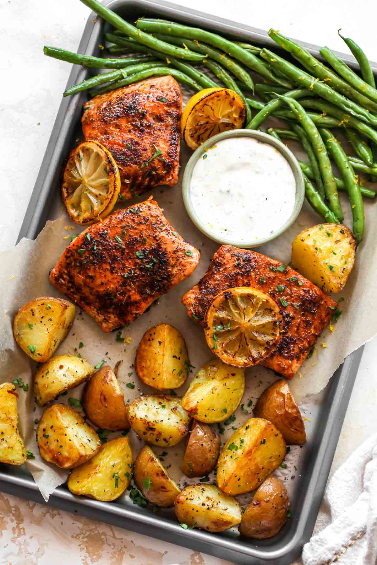 Salmon, roasted potatoes, green beans, and herb sauce on a silver baking sheet as part of a spring dinner recipe collection.