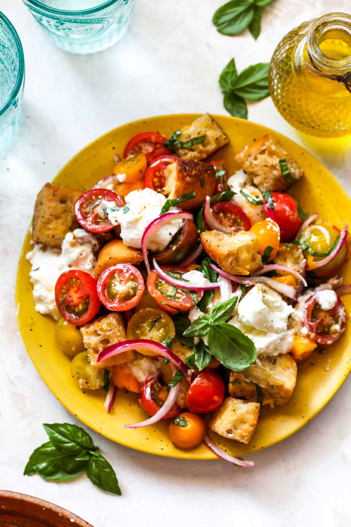 One portion of Panzanella salad served on a yellow plate topped with fresh basil leaves.