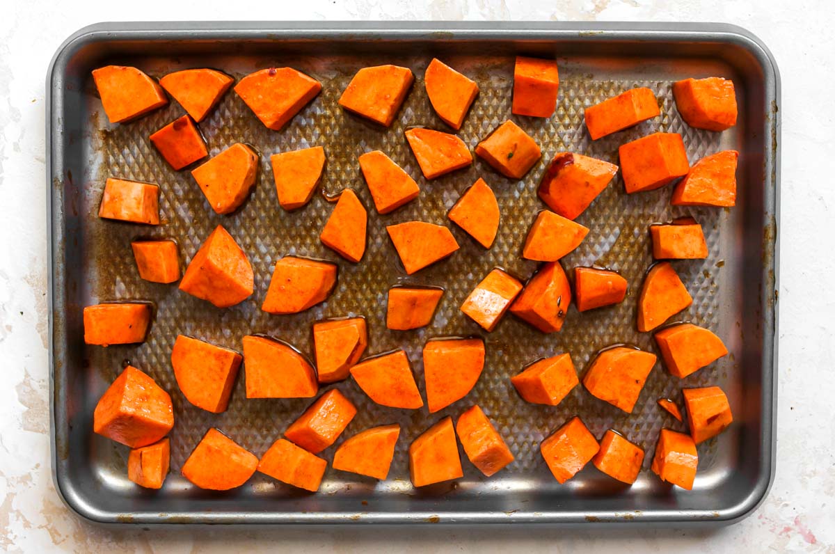 Cubes of sweet potatoes tossed in oil and spices on a baking sheet