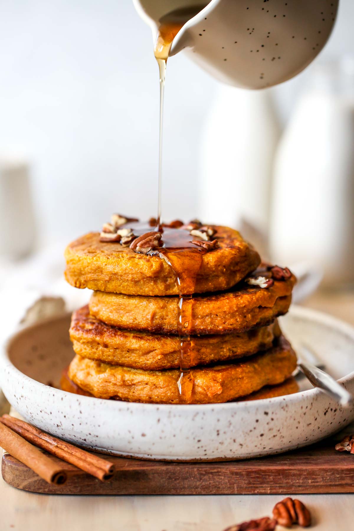 Stack of pumpkin protein pancakes being drizzled with maple syrup on a white plate.