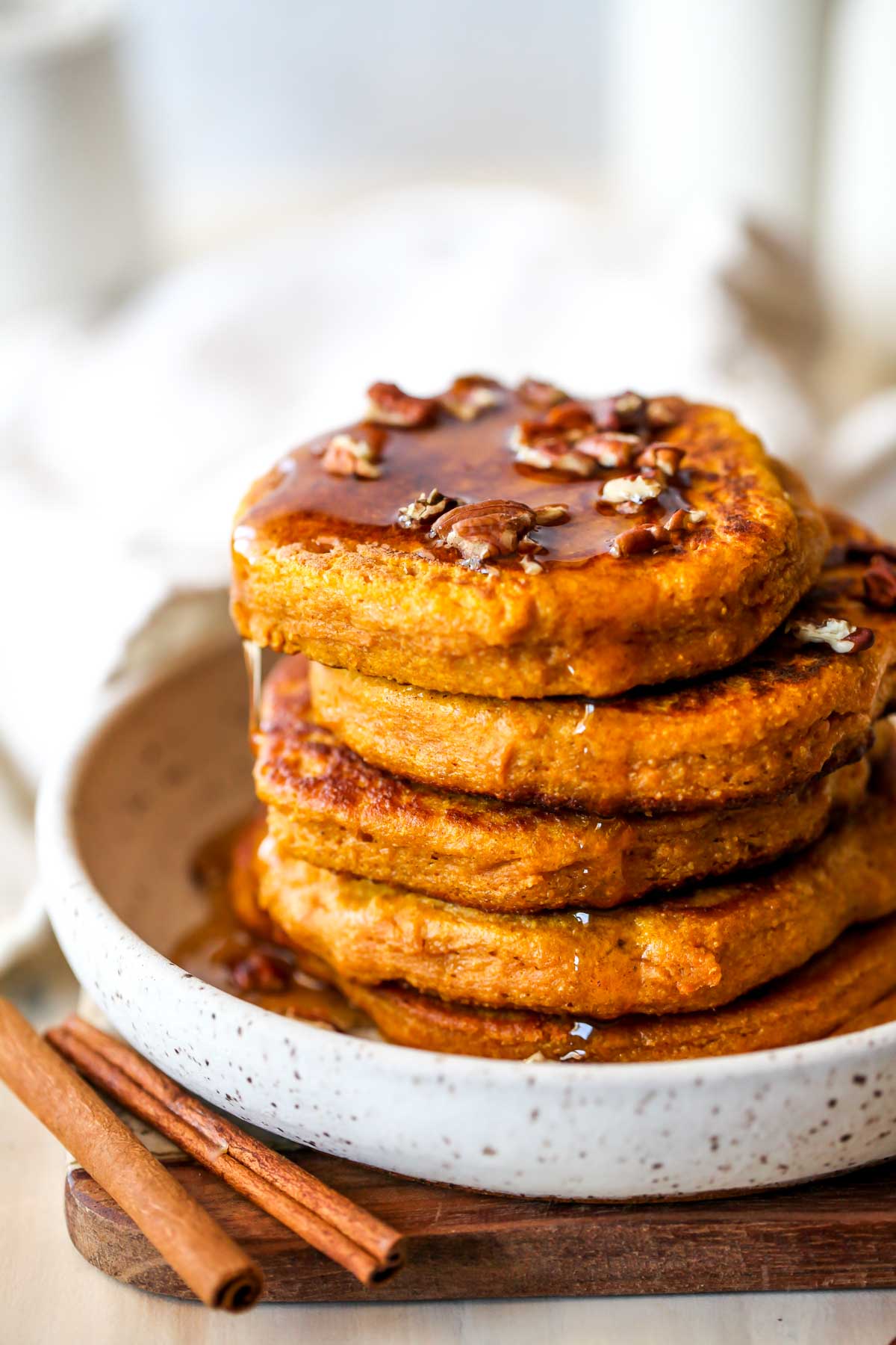 Stack of pumpkin pancakes topped with pecans and maple syrup on a white plate.