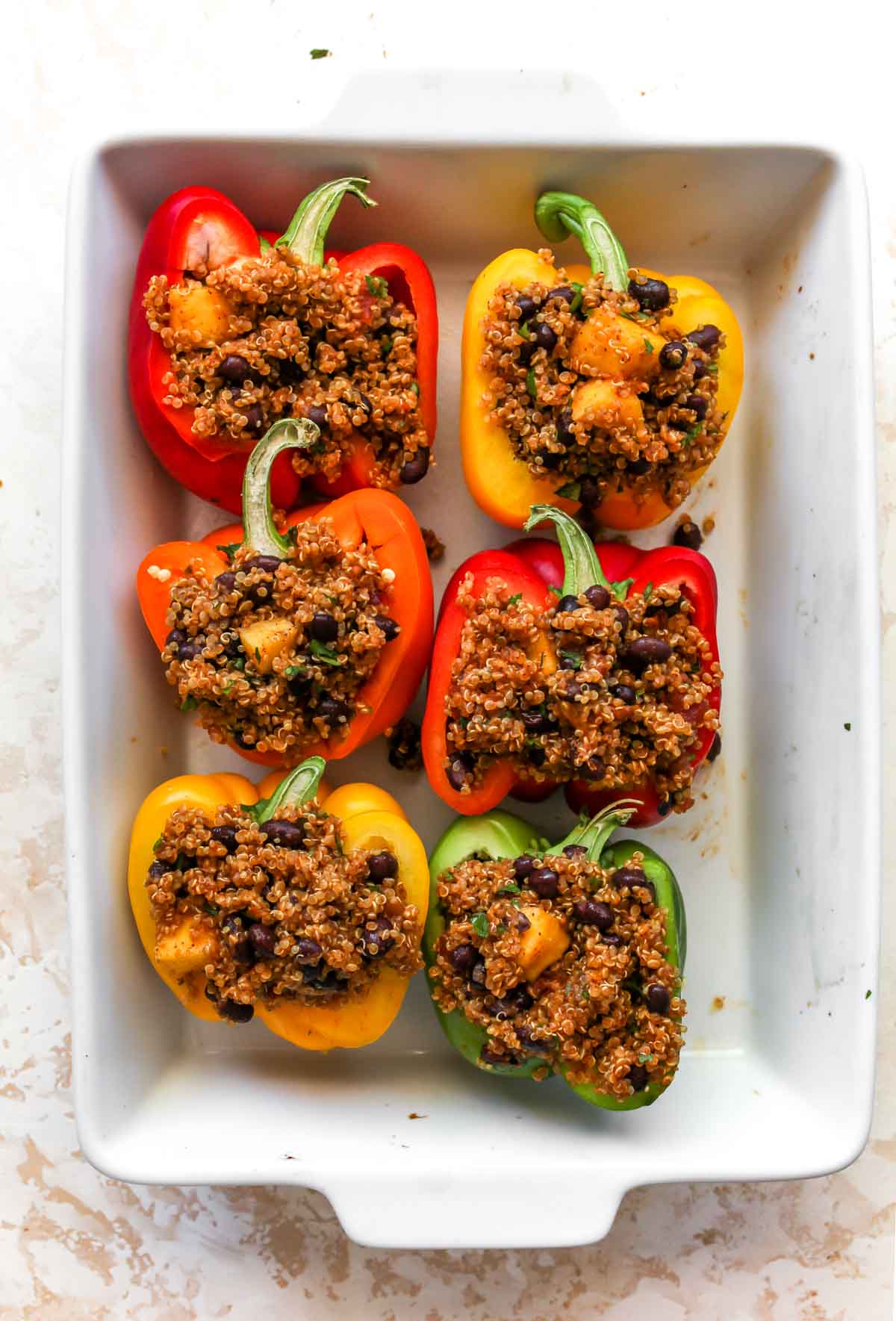Bell pepper halves filled with quinoa and black beans in a white pan
