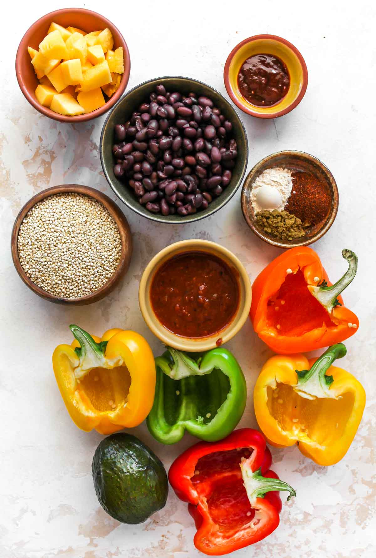 Bell pepper halves, black beans, quinoa, and spices in separate bowls on a white board