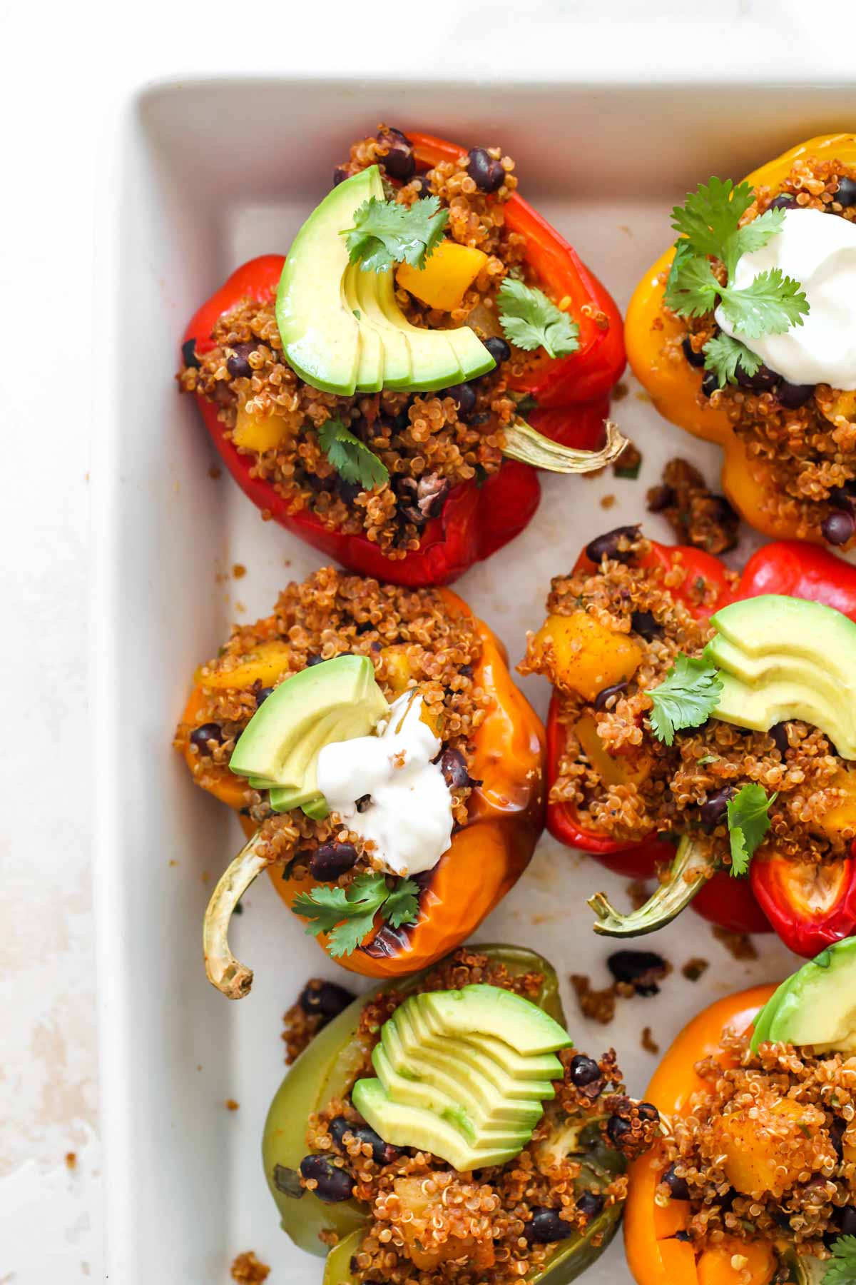 Quinoa stuffed peppers topped with avocado and cilantro in a baking pan