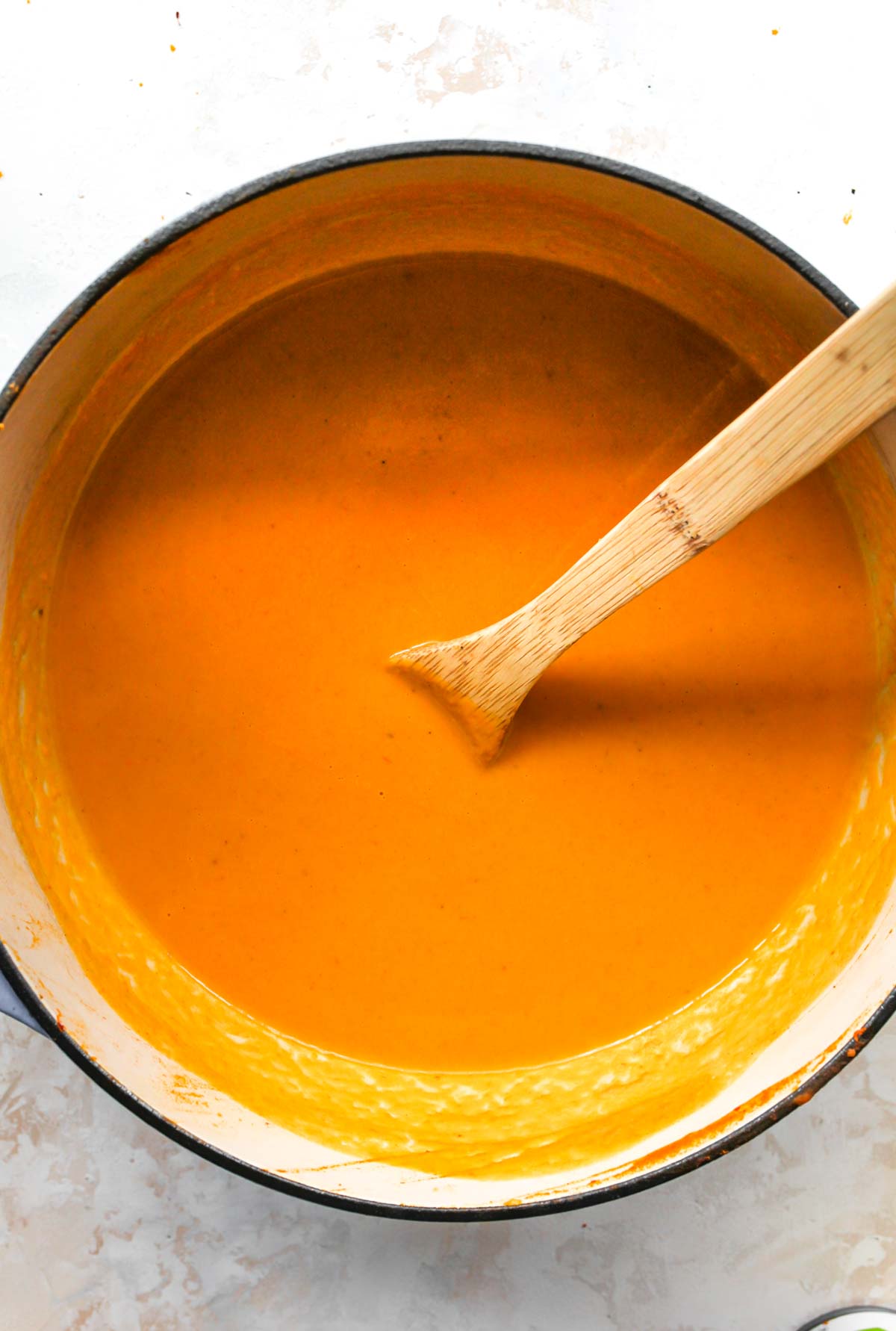 A wooden spoon stirring pumpkin soup in a Dutch oven