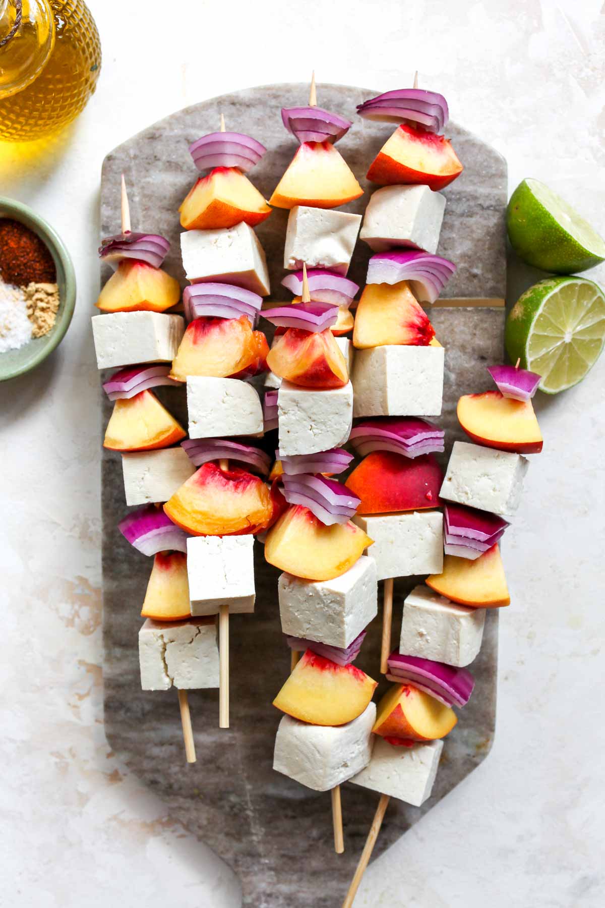 Tofu, peaches, and onion being put on wood kebabs