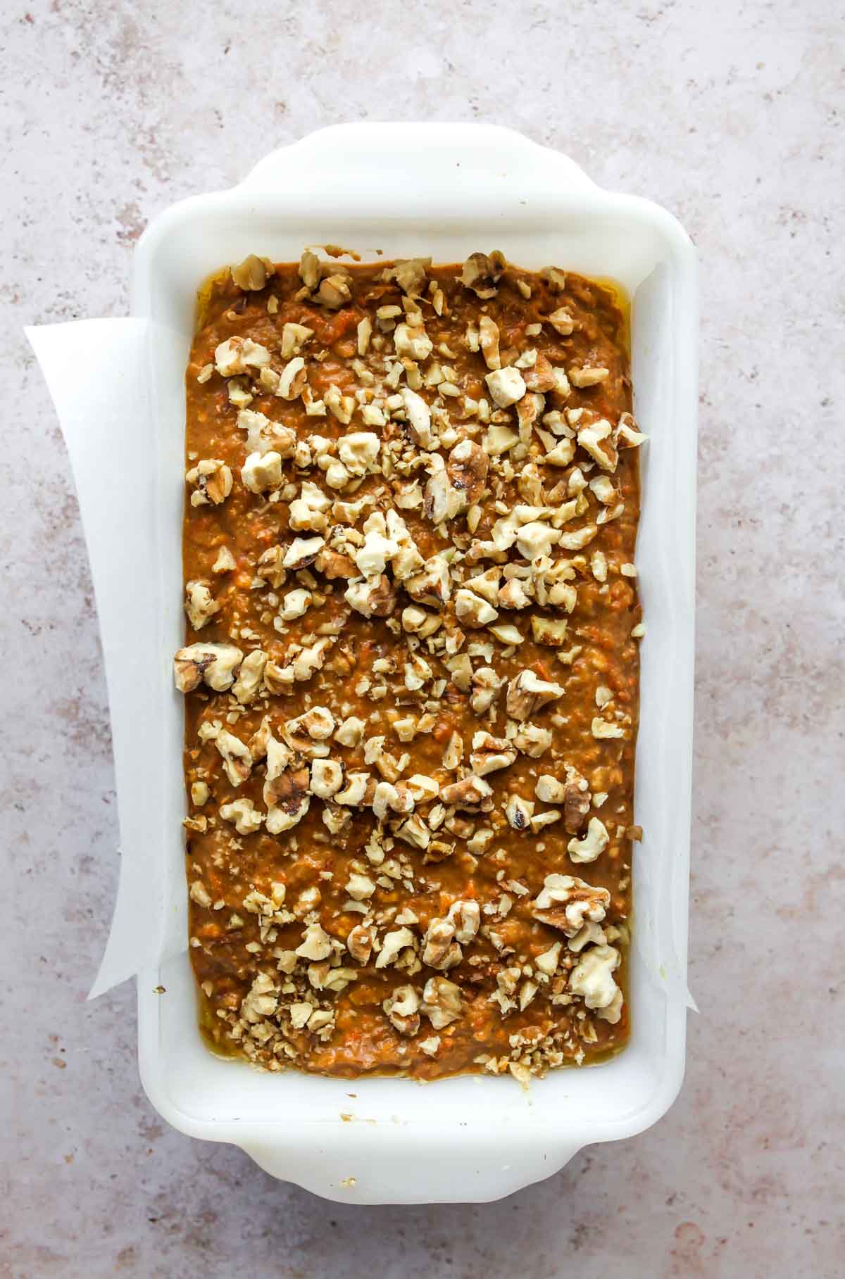 Bread batter being added to a loaf pan and topped with walnuts