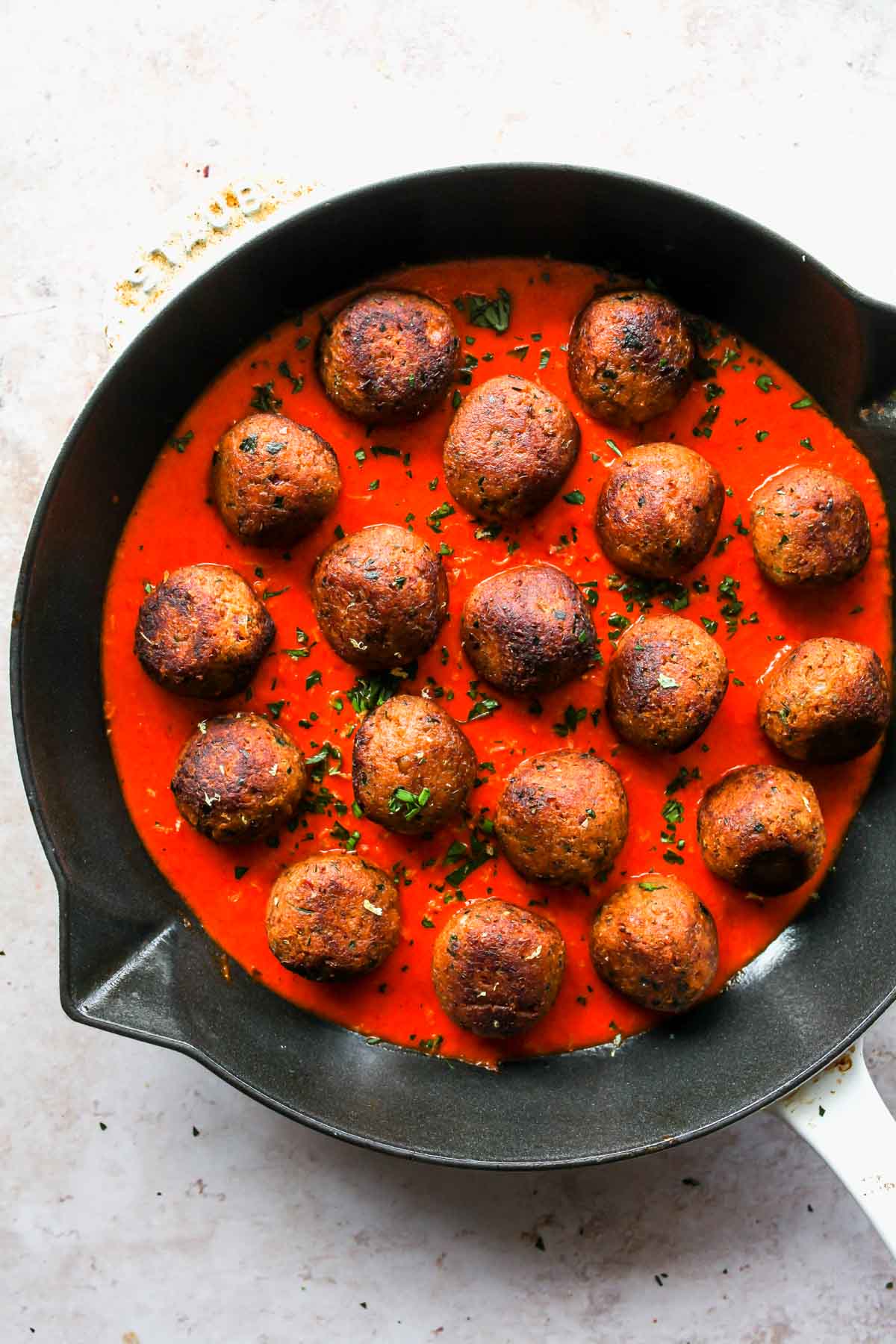 Lentil meatballs in a skillet topped with roasted red pepper sauce
