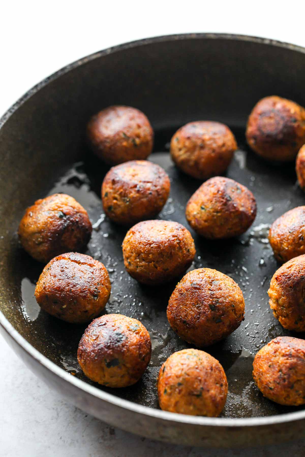 Lentil meatballs being seared in a large black skillet