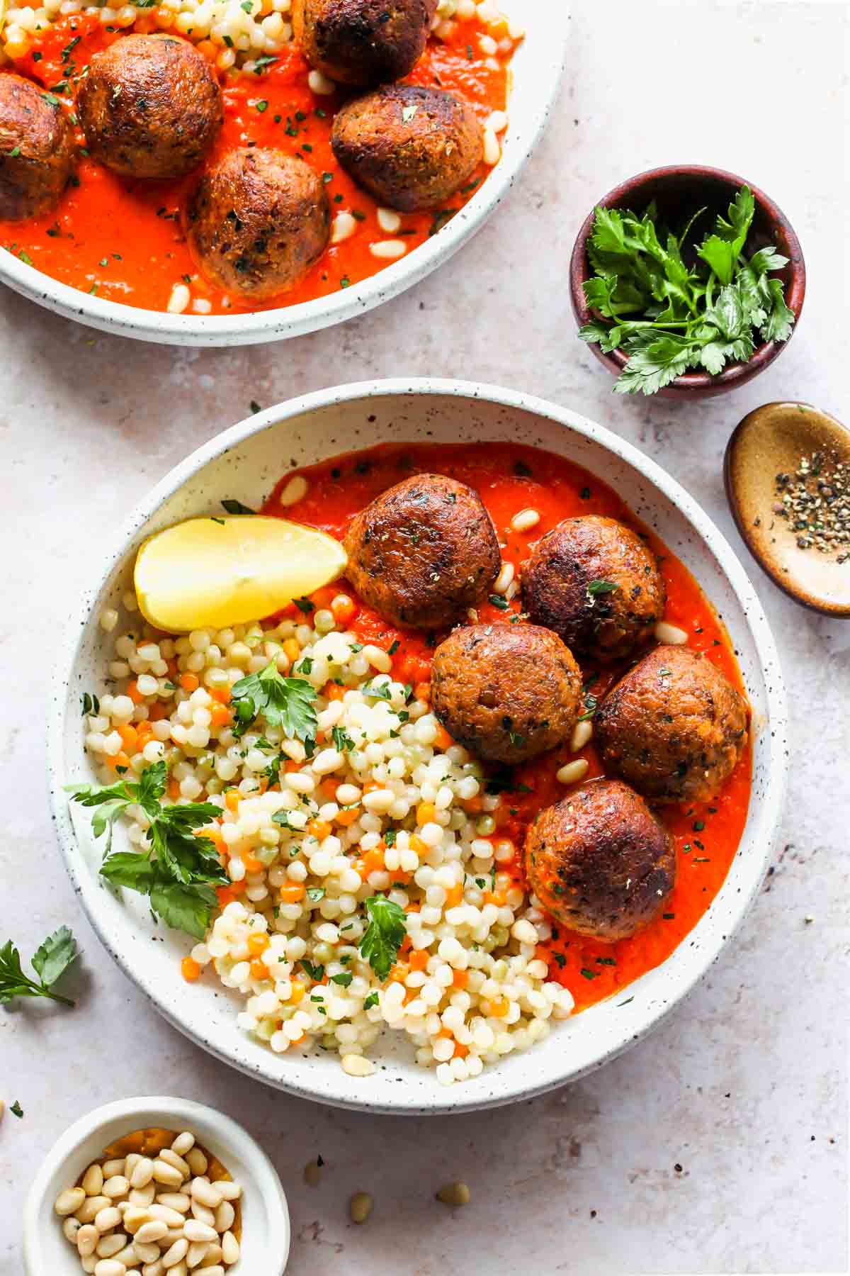 Moroccan meatballs and pearl couscous in a white bowl with lemon garnish