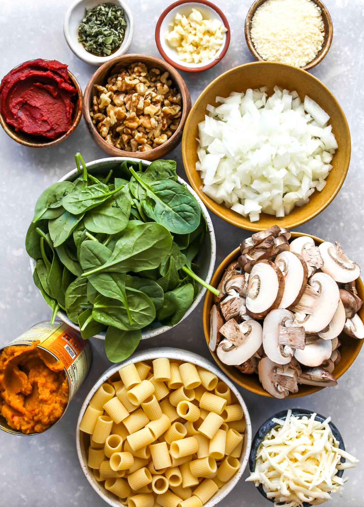 Pumpkin pasta bake ingredients in separate bowls on a gray surface.