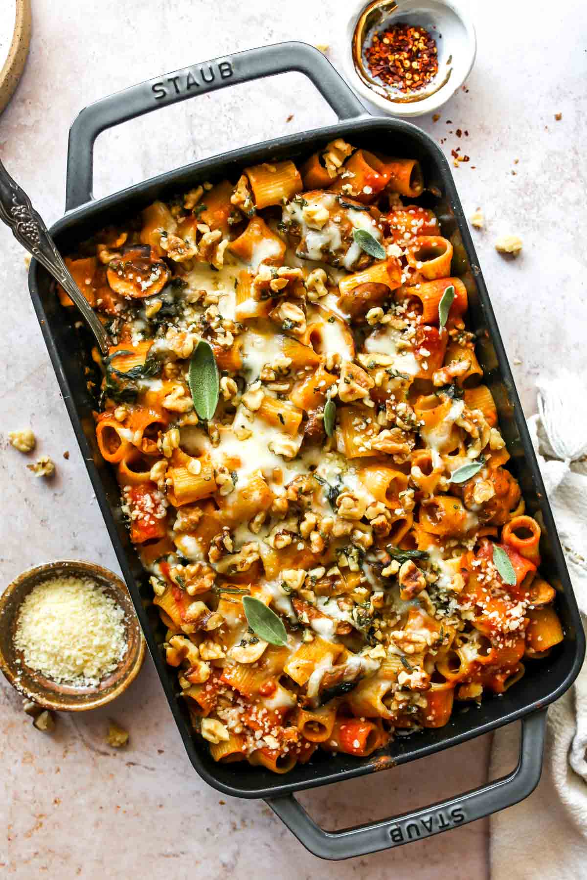 Cheesy pumpkin pasta in a baking dish topped with walnuts and sage.