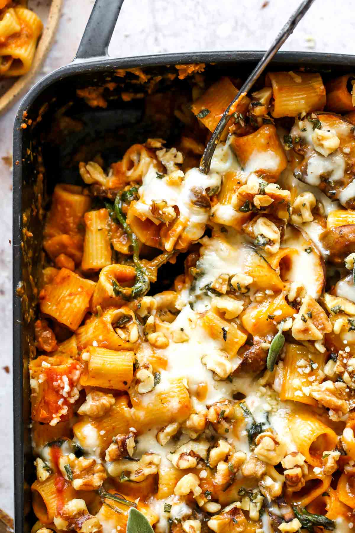 Serving spoon digging into a pan of pumpkin baked pasta.