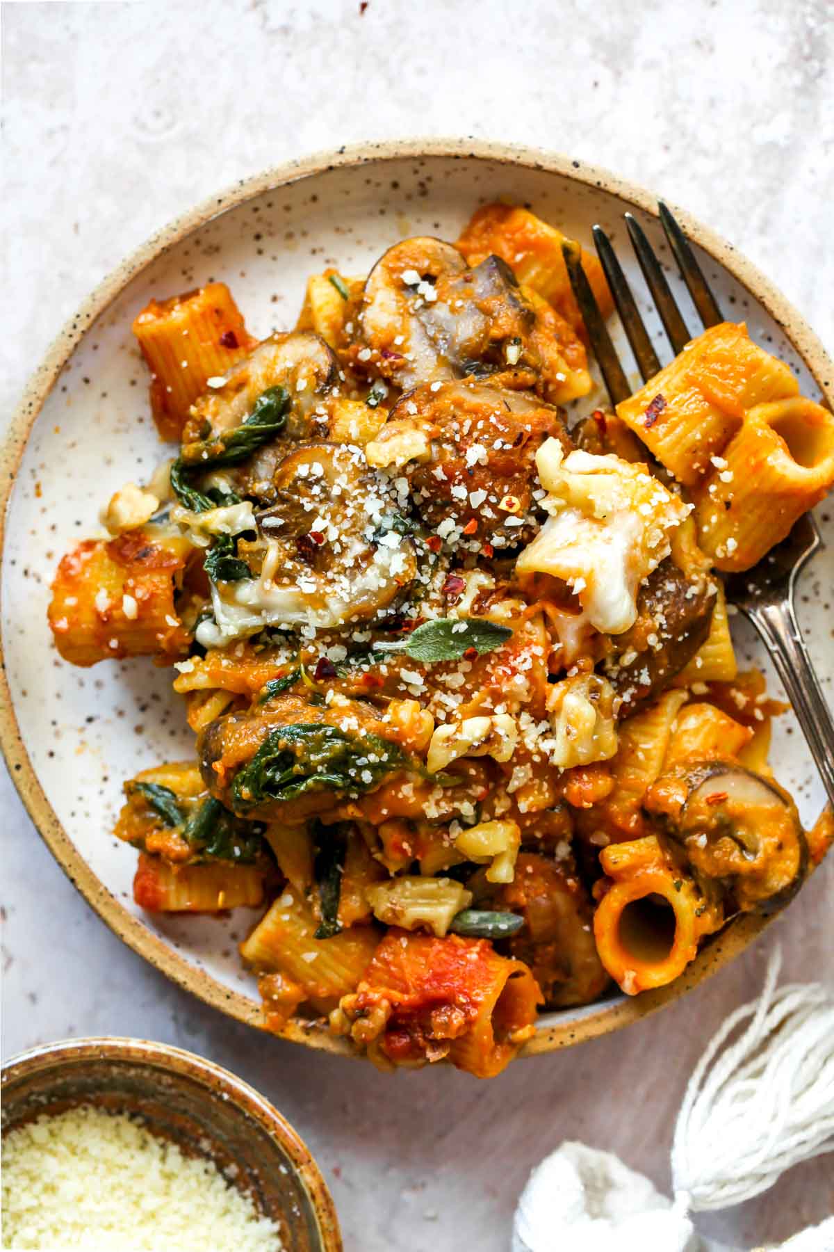 One serving of baked pumpkin pasta styled on a small white plate topped with sage, walnuts, and Parmesan.
