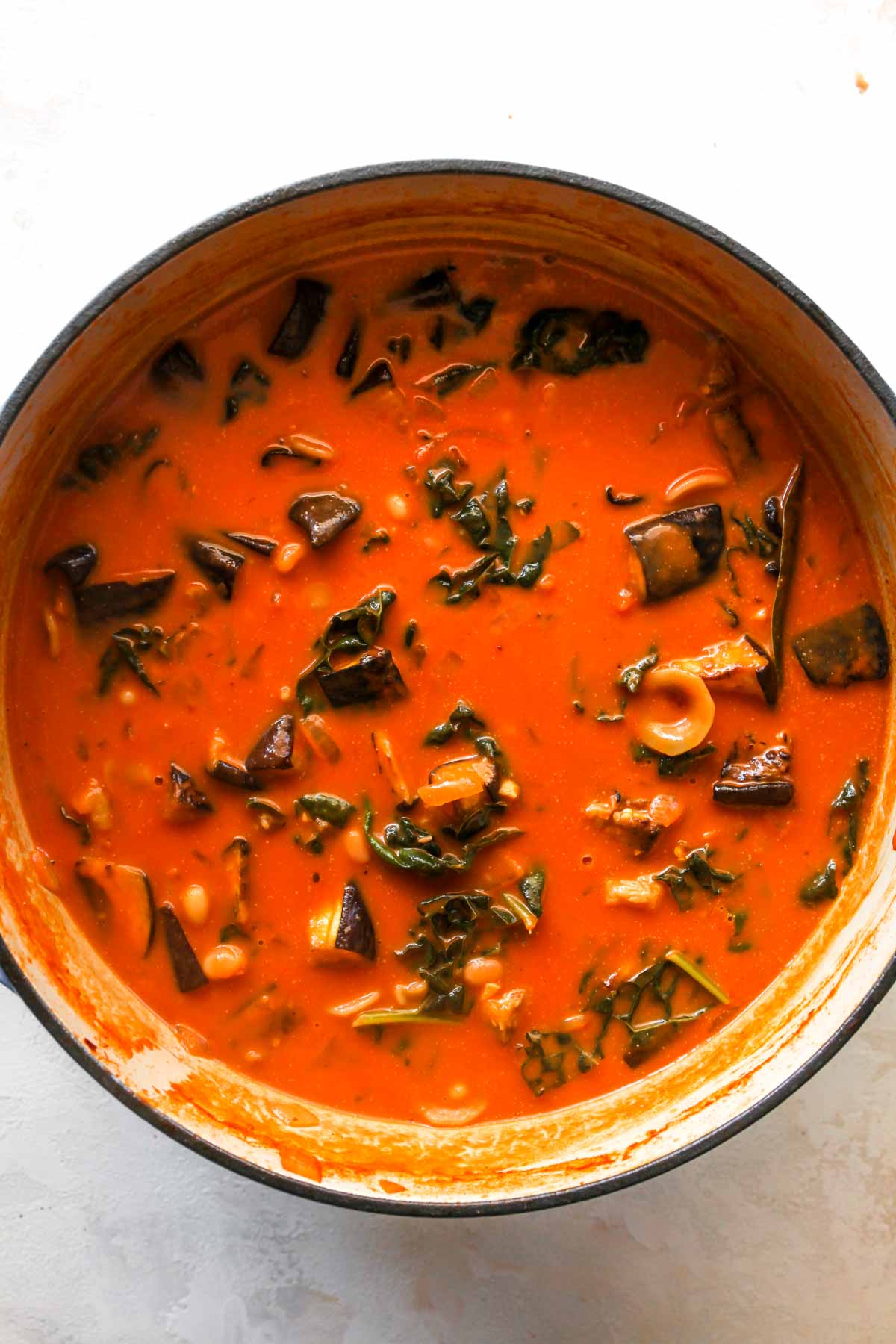Cream and cheese being added to a pot of eggplant and tomato soup