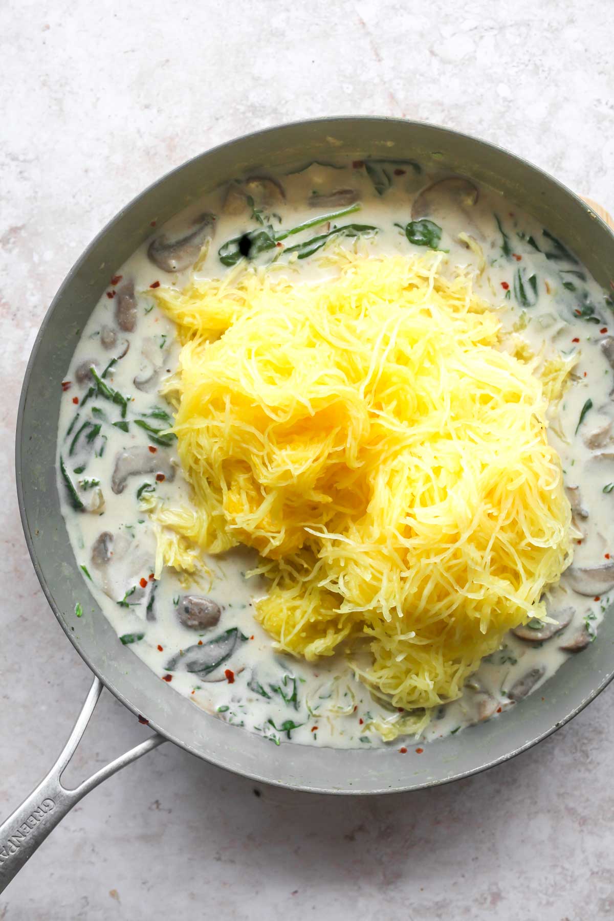 Strands of spaghetti squash being mixed into a skillet of goat cheese sauce
