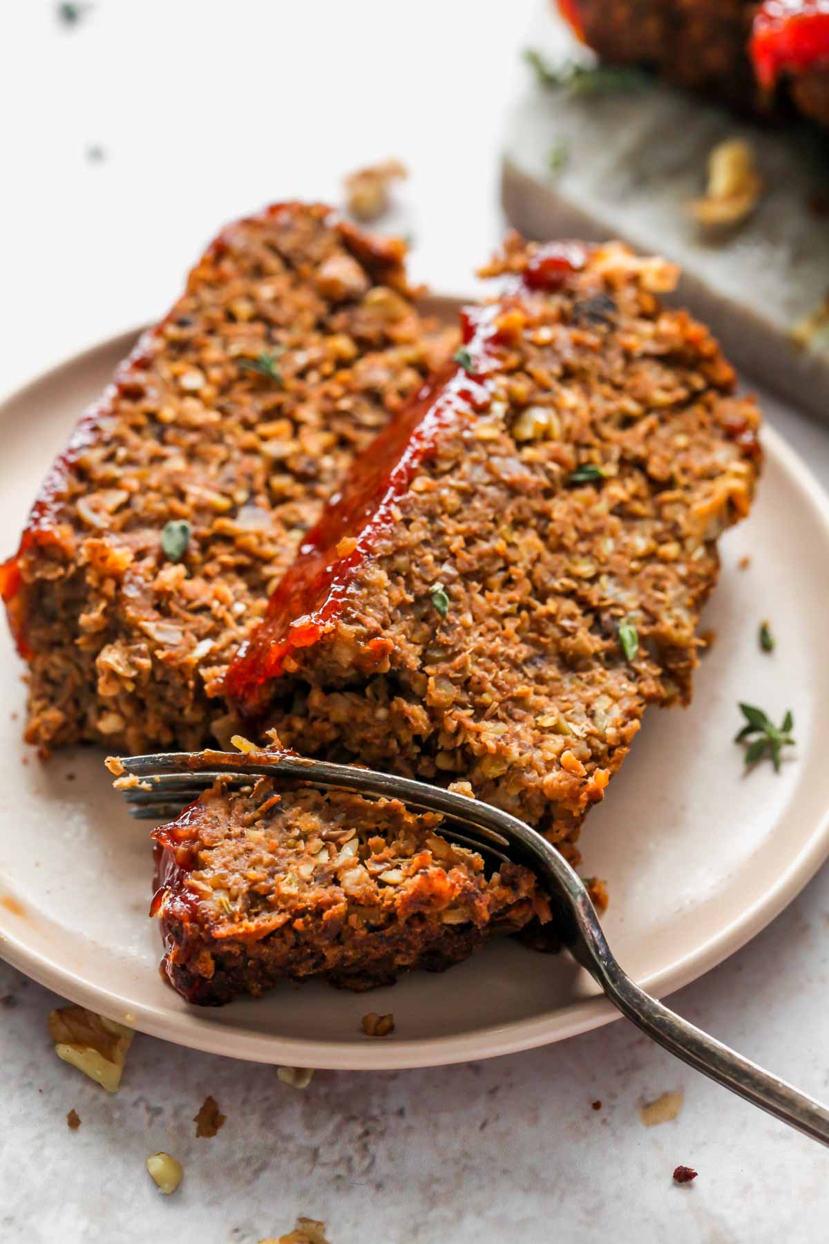Two slices of vegan meatloaf on a peach plate with a fork slicing off a bite