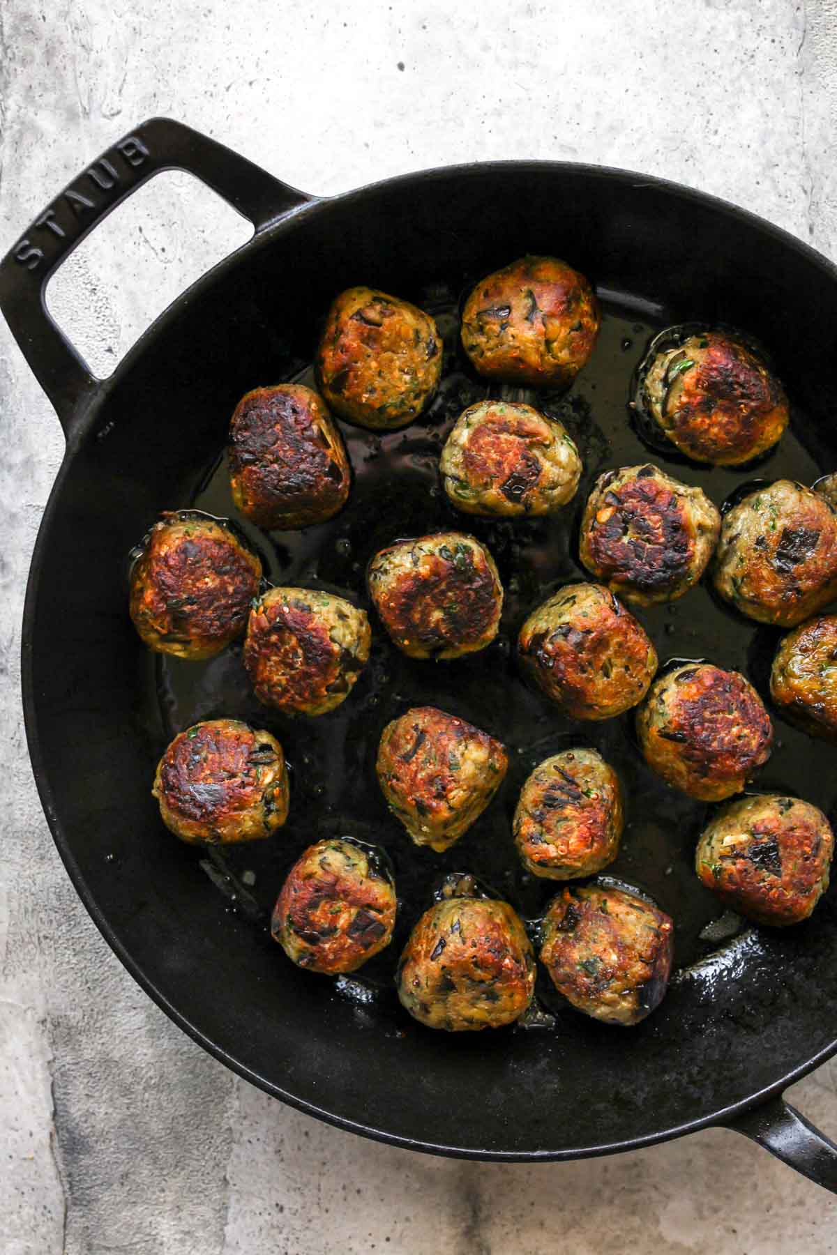Eggplant meatballs being sautéed until golden in a cast iron skillet.