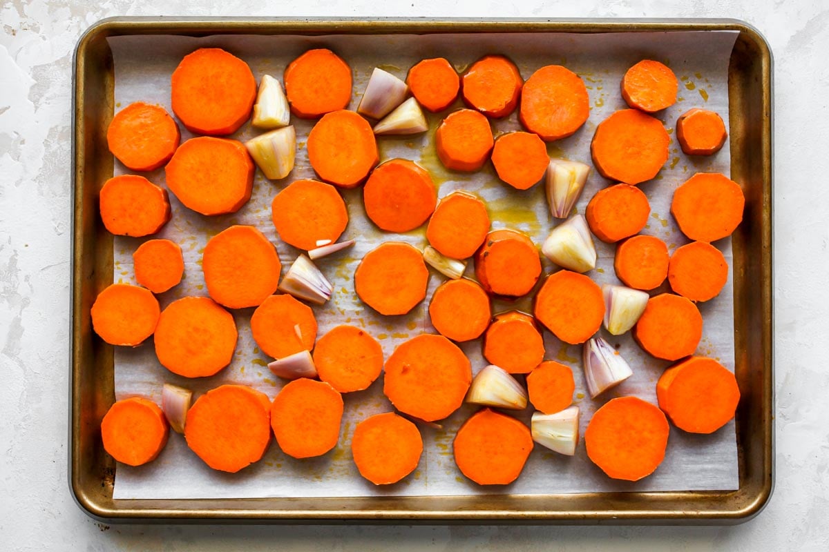 Sweet potato coins and shallots tossed in oil on a baking sheet