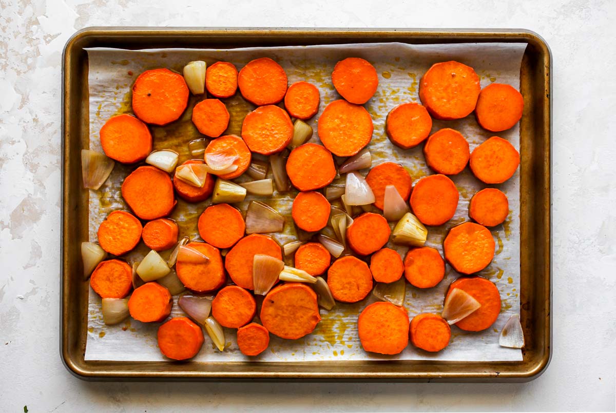 Sweet potatoes and shallots tossed in maple butter on a baking sheet