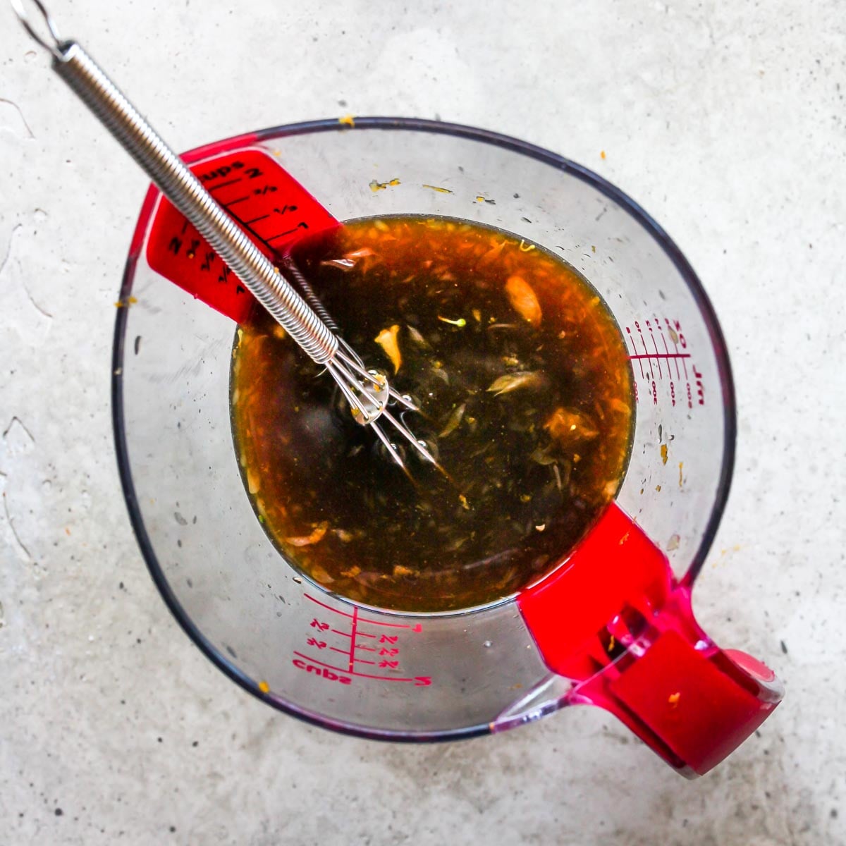Soy sauce, vinegar, and orange juice being whisked in a glass measuring cup