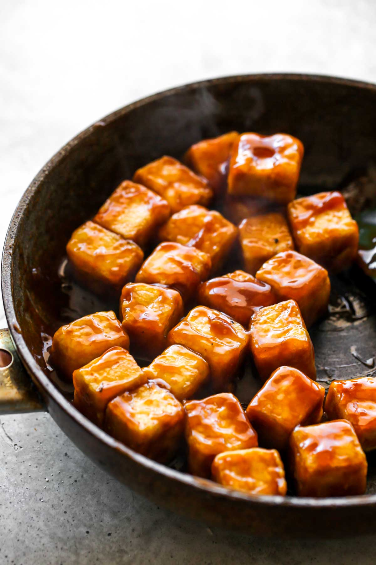 Tofu cubes being coated in orange sauce in a skillet